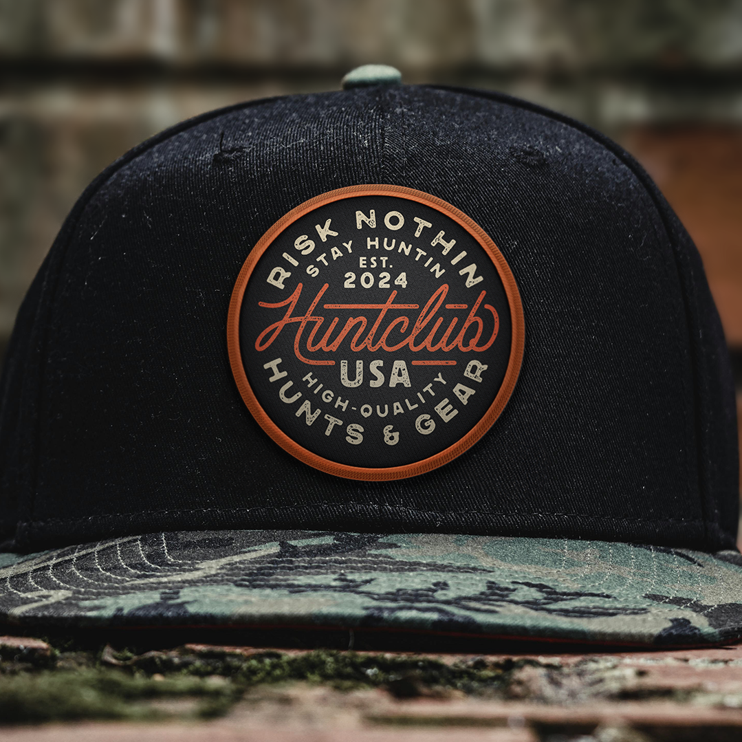Custom hunting patch logo design for Huntclub USA displayed on a camo brim hat with vintage outdoor branding and apparel-focused badge design.