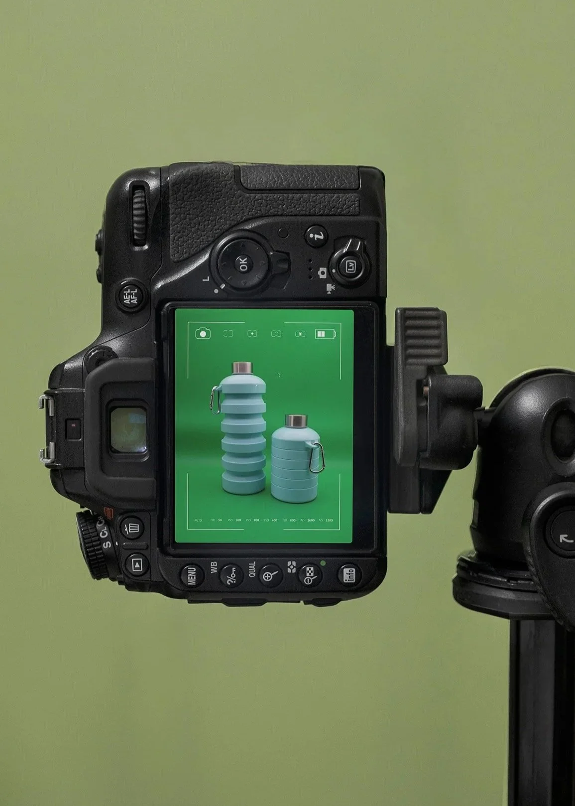 Digital camera on a tripod capturing an image of four blue storage tanks with silver caps and attached carabiners against a green background.