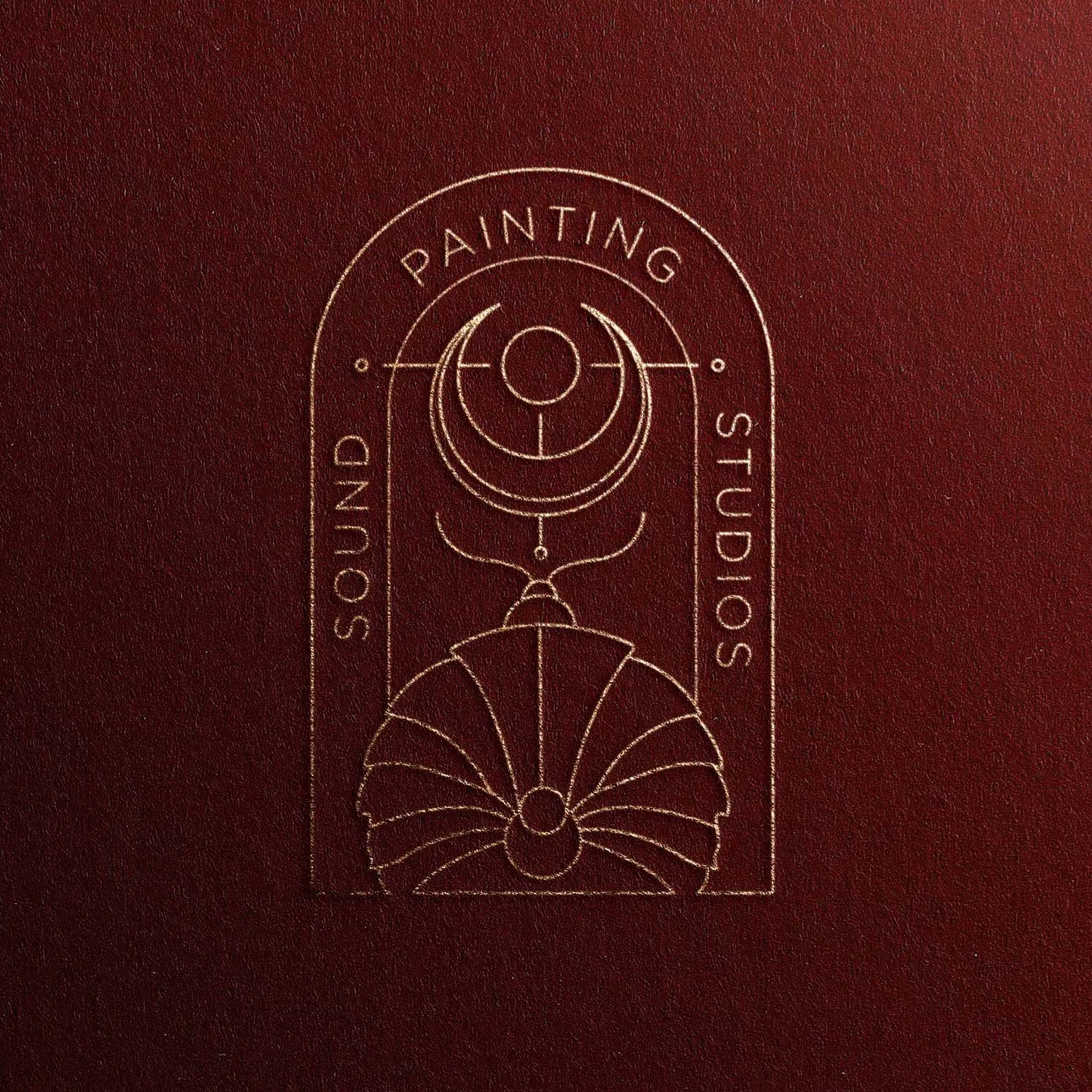Gold embossed logo for Sound Painting Studio on dark red surface, featuring geometric and line art design.