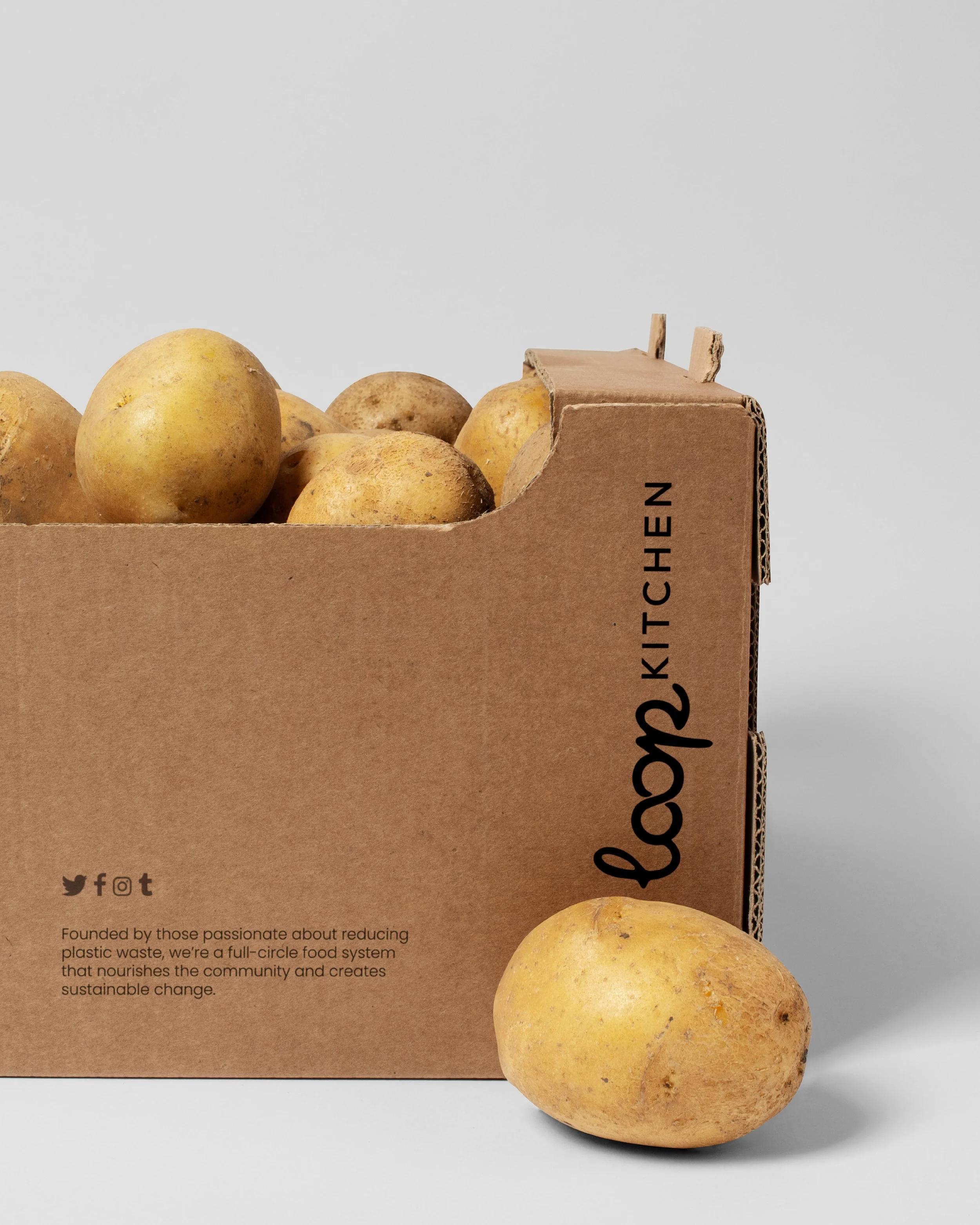 A cardboard box labeled 'The Loop Kitchen' filled with yellow potatoes, with one potato outside the box.
