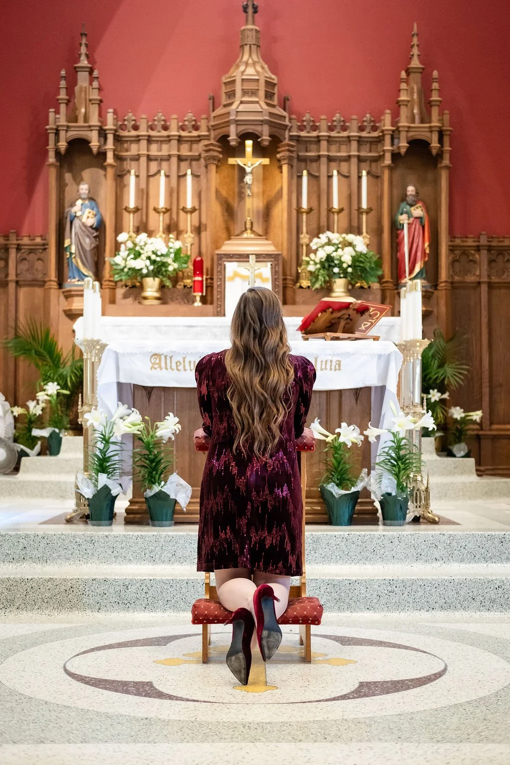 Madigan kneels in prayer before the altar in a Catholic church, reflecting discernment, reverence, and prayerful care for her matchmaking work.