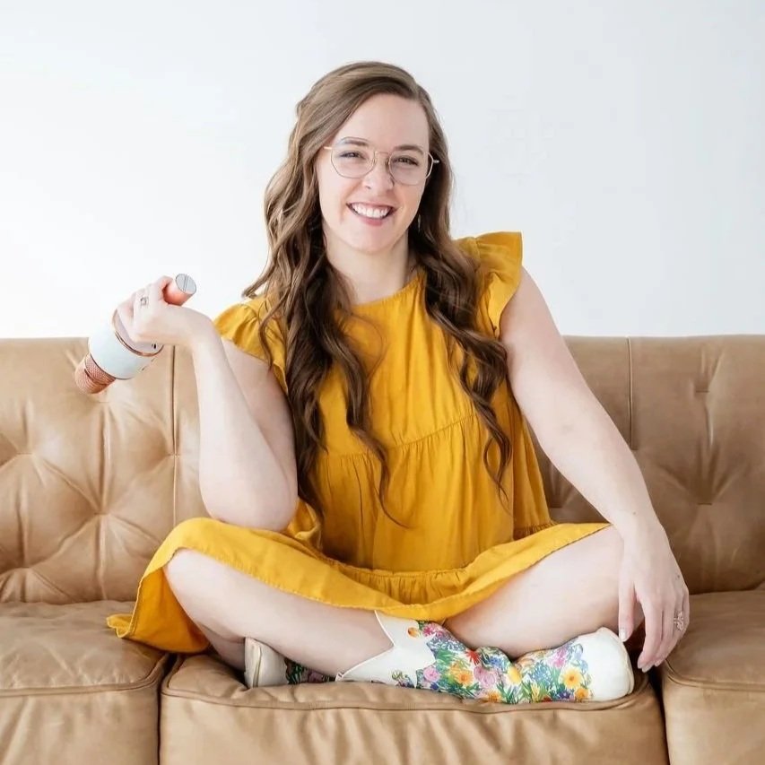 Madigan, founder of CommitmentISM, sits casually on a couch, smiling with an open and approachable expression.