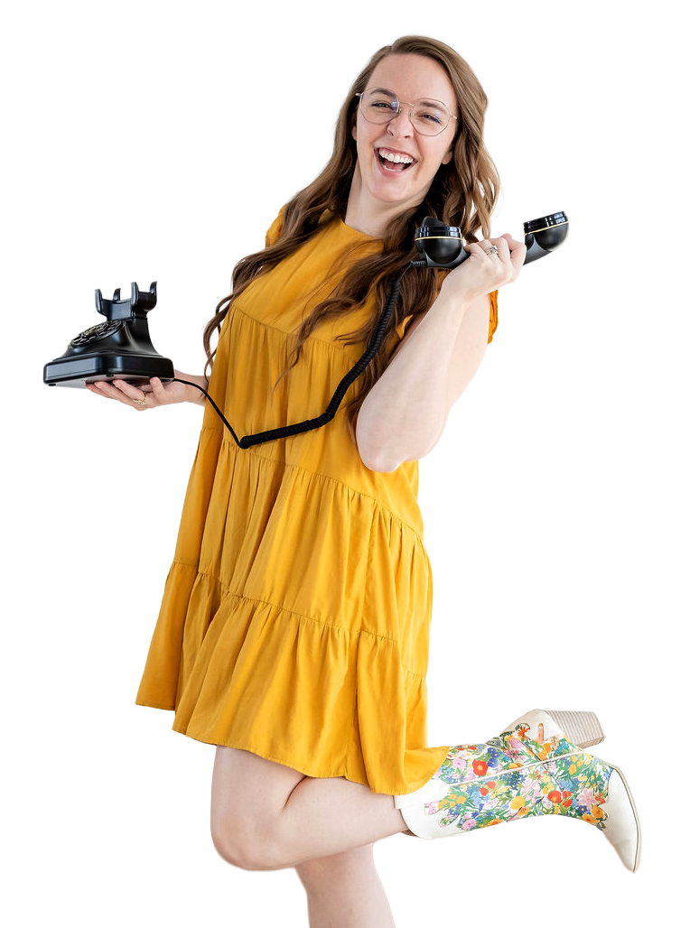 Madigan, founder of CommitmentISM, laughs while holding a vintage phone, conveying warmth, approachability, and an open invitation to connect.