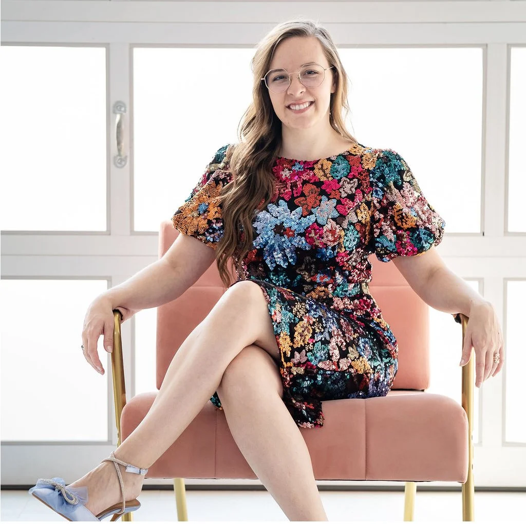 Madigan, founder of CommitmentISM, sits confidently in a chair, smiling warmly and conveying trust and approachability.