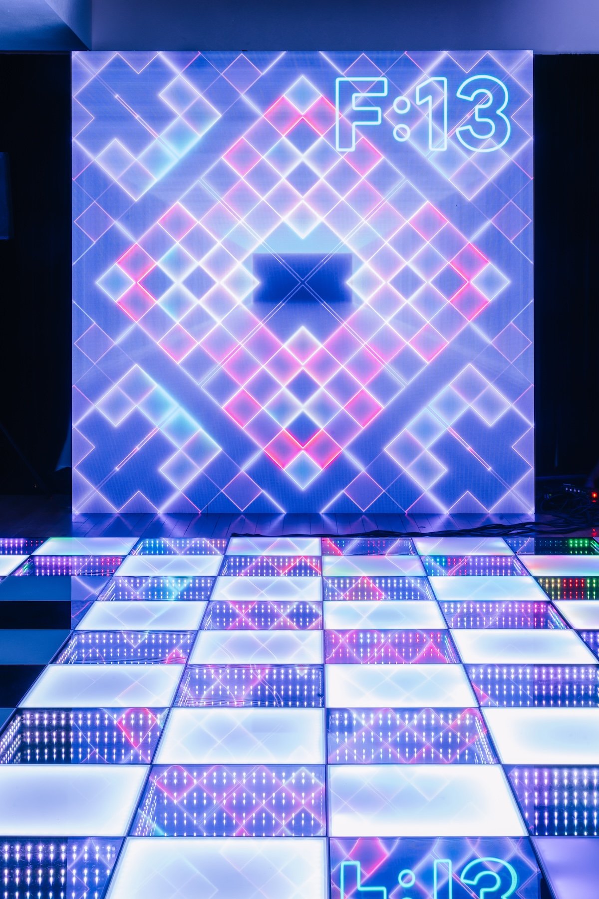 Illuminated LED dance floor with lounge seating and custom “F:13” neon backdrop at modern arcade themed 13th birthday party