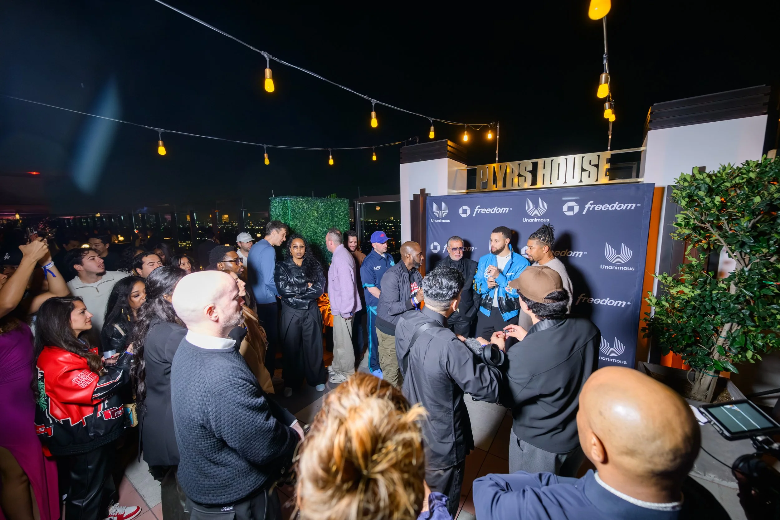 Guests posing beside curated Unanimous Media display wall during Stephen Curry’s All-Star Weekend rooftop experience produced by Loriann Serna of The Wife of the Party.
