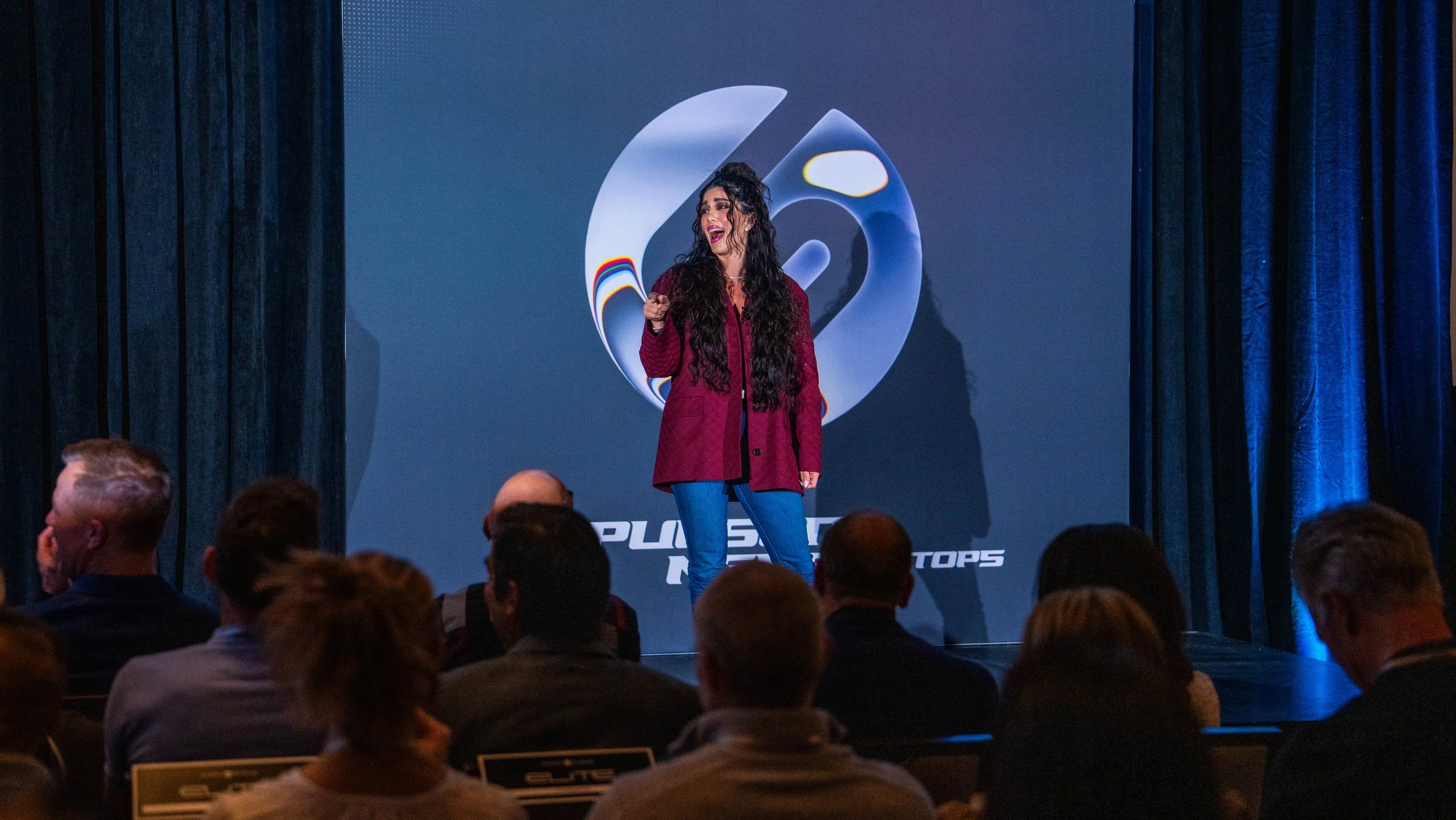 Speaker Nineveh Madsen presenting on stage at the Supra Human Elite Fly-In event featuring branded staging and lighting produced by Wife of the Party.