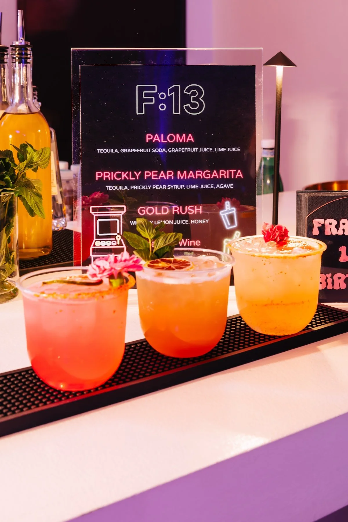 Signature cocktails including prickly pear margarita and paloma displayed at neon arcade themed birthday party bar by Wife of the Party