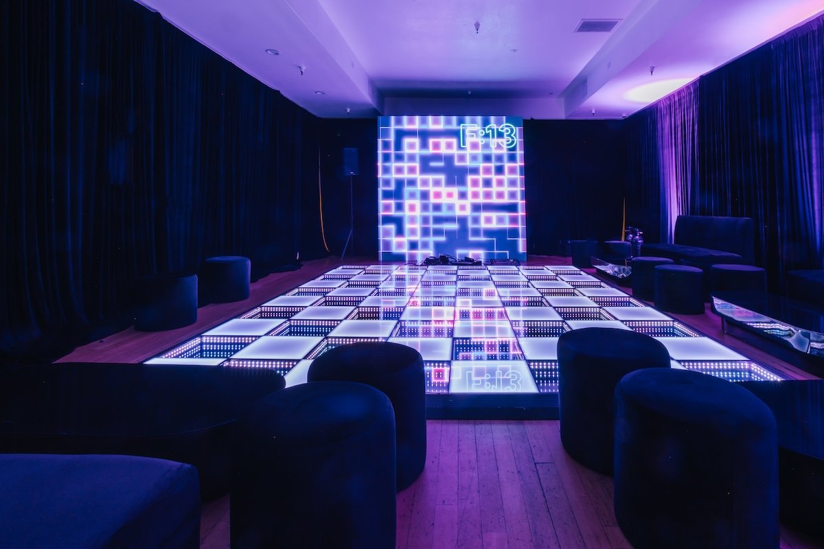 Illuminated LED dance floor with lounge seating and custom “F:13” neon backdrop at modern arcade themed 13th birthday party by Wife of the Party