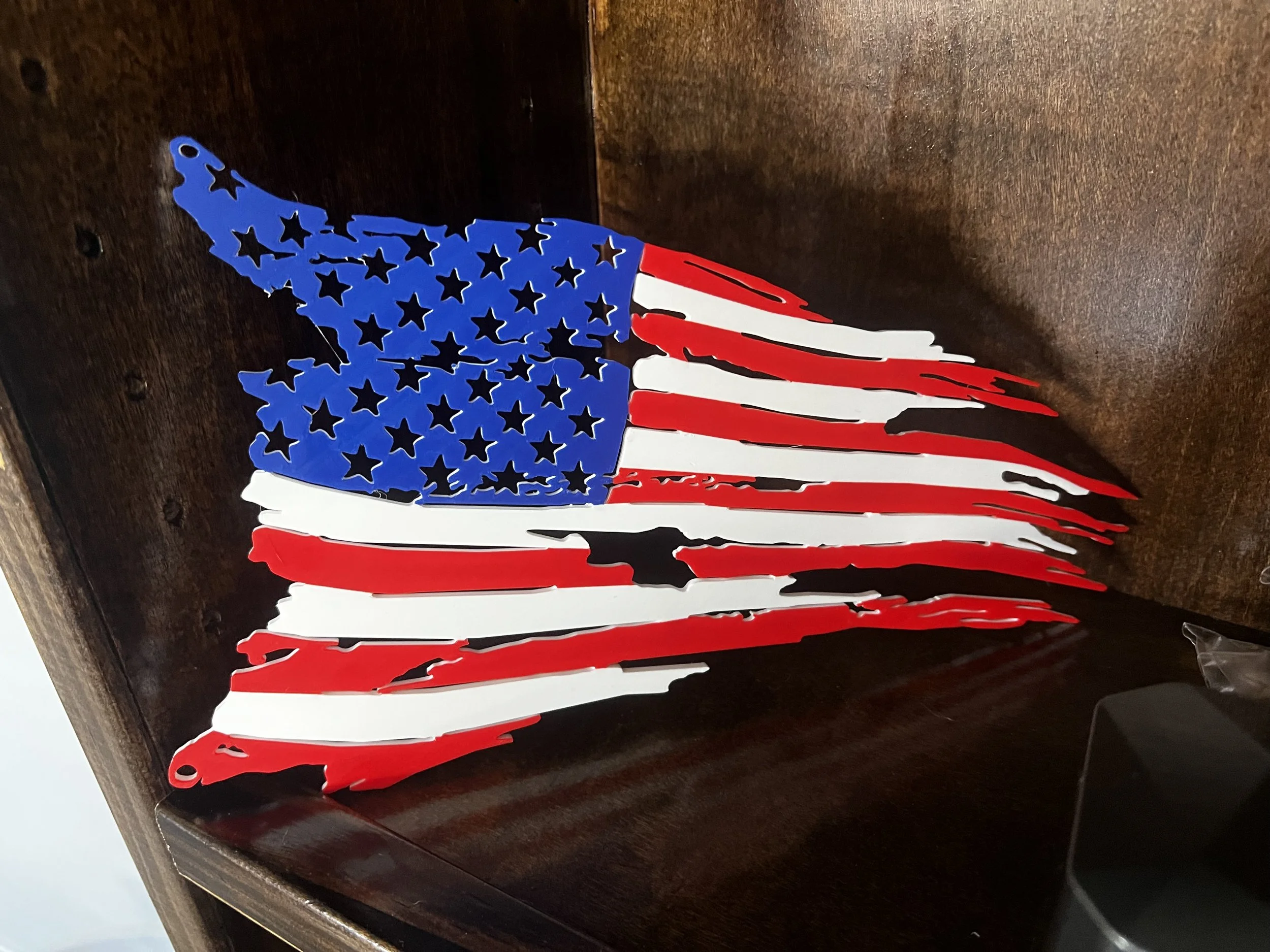 Decorative American flag with blue stars and red and white stripes hanging on a dark brown wall or shelf.