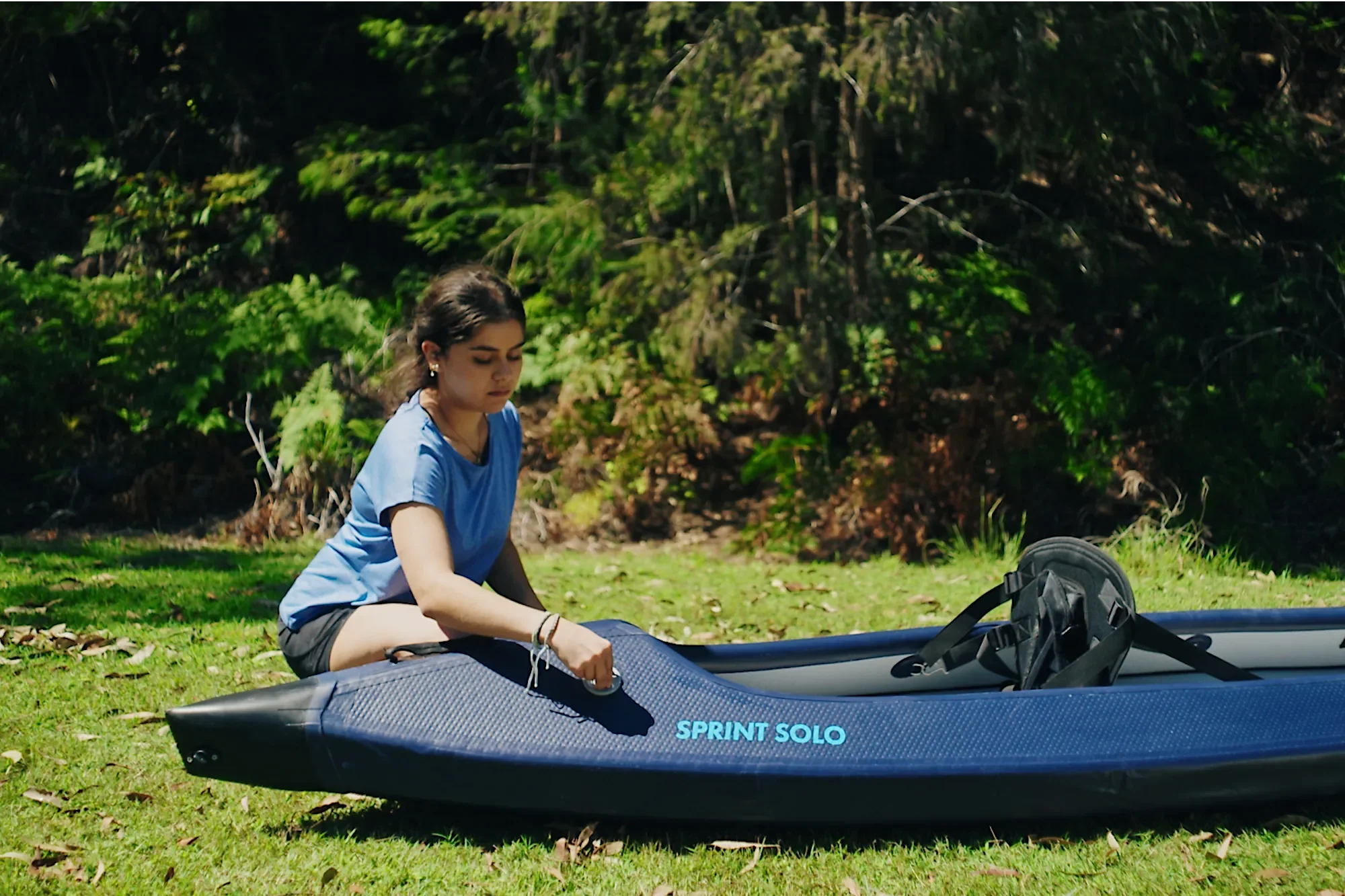 Femme installant un kayak gonflable orange Razor Kayaks Sprint Solo dans un parc.