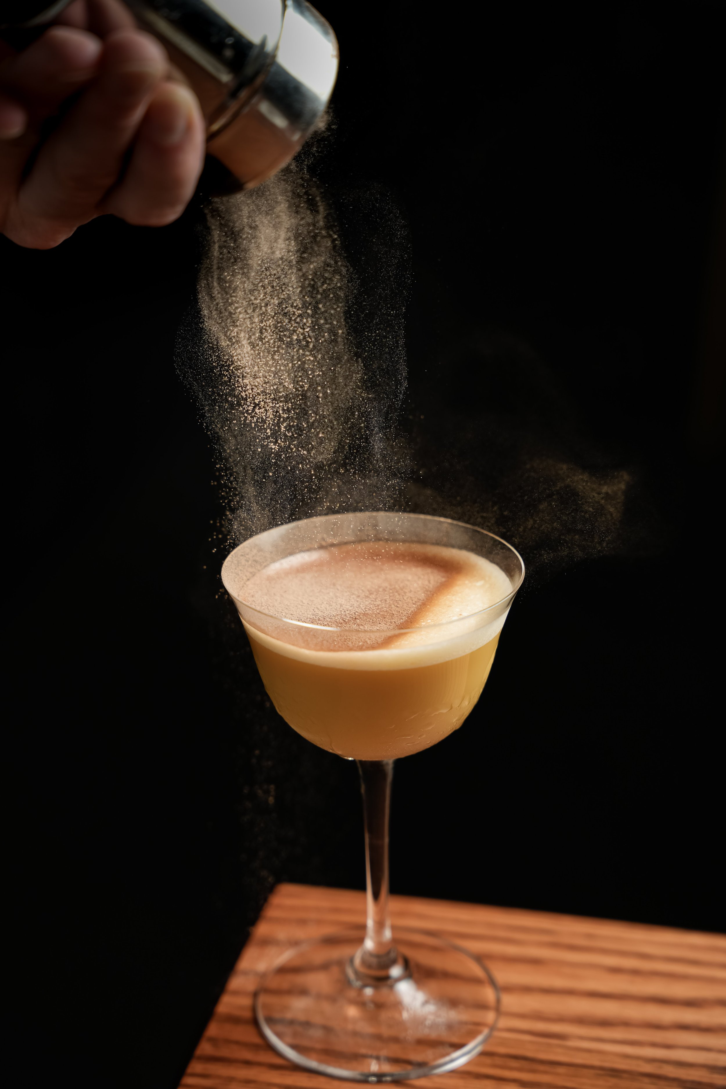 A bartender sprinkles powdered sugar onto a pink cocktail in a martini glass