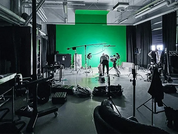 A film or video production studio with a green screen backdrop, cameras, lighting, and crew setting up equipment.