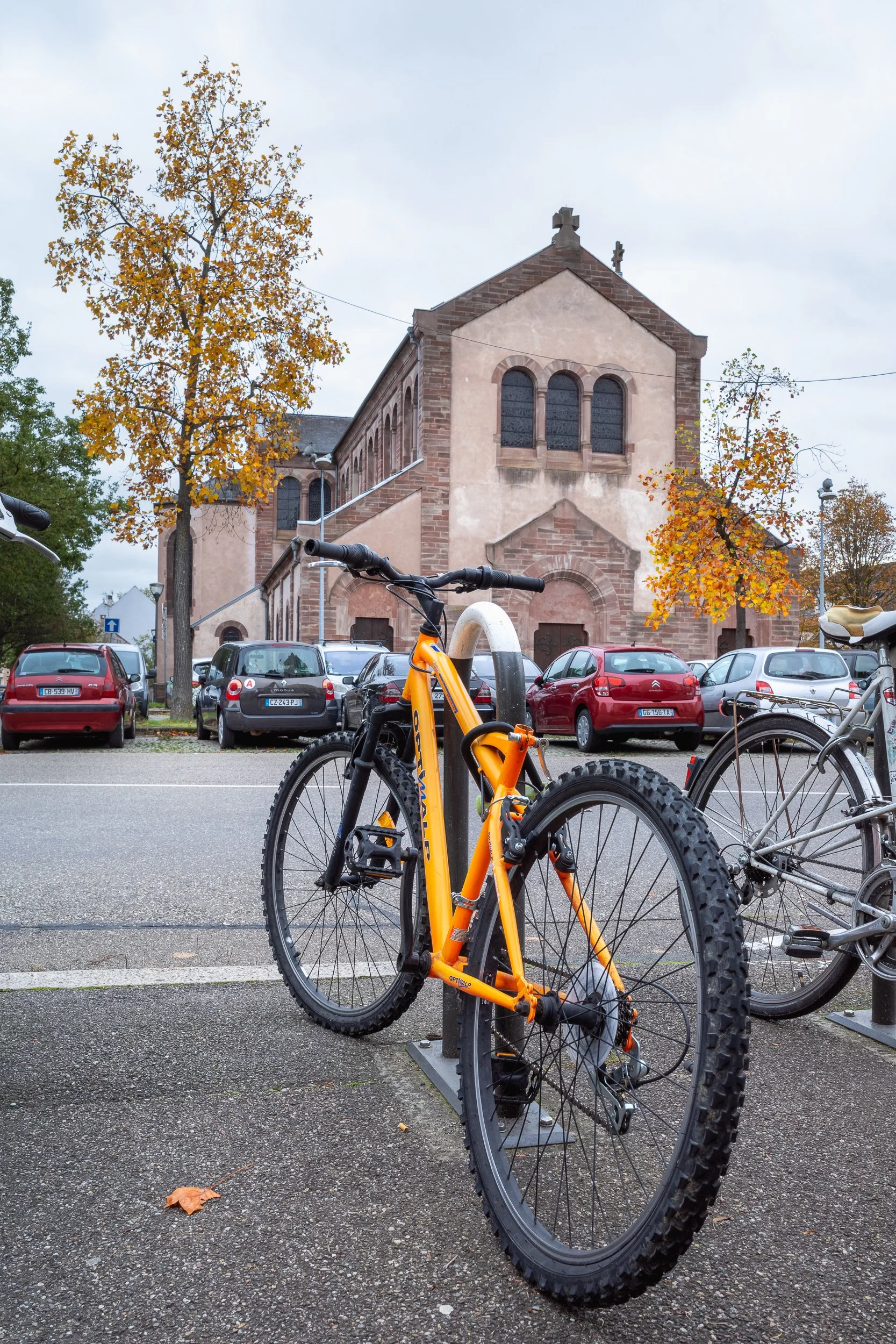 Orange bicycle parked near a church and autumn trees in Strasbourg.