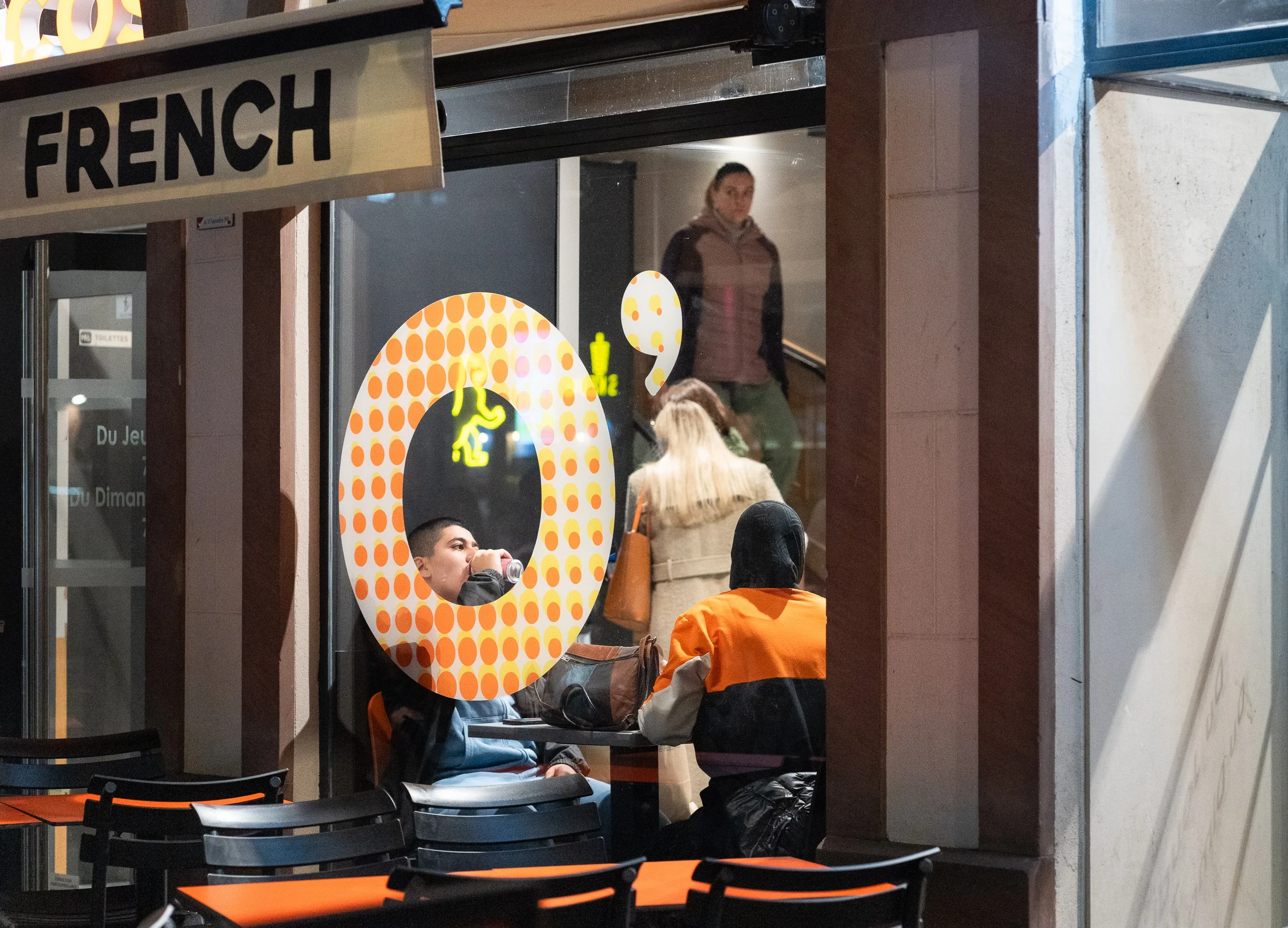 People sitting inside a café framed by orange window graphics.