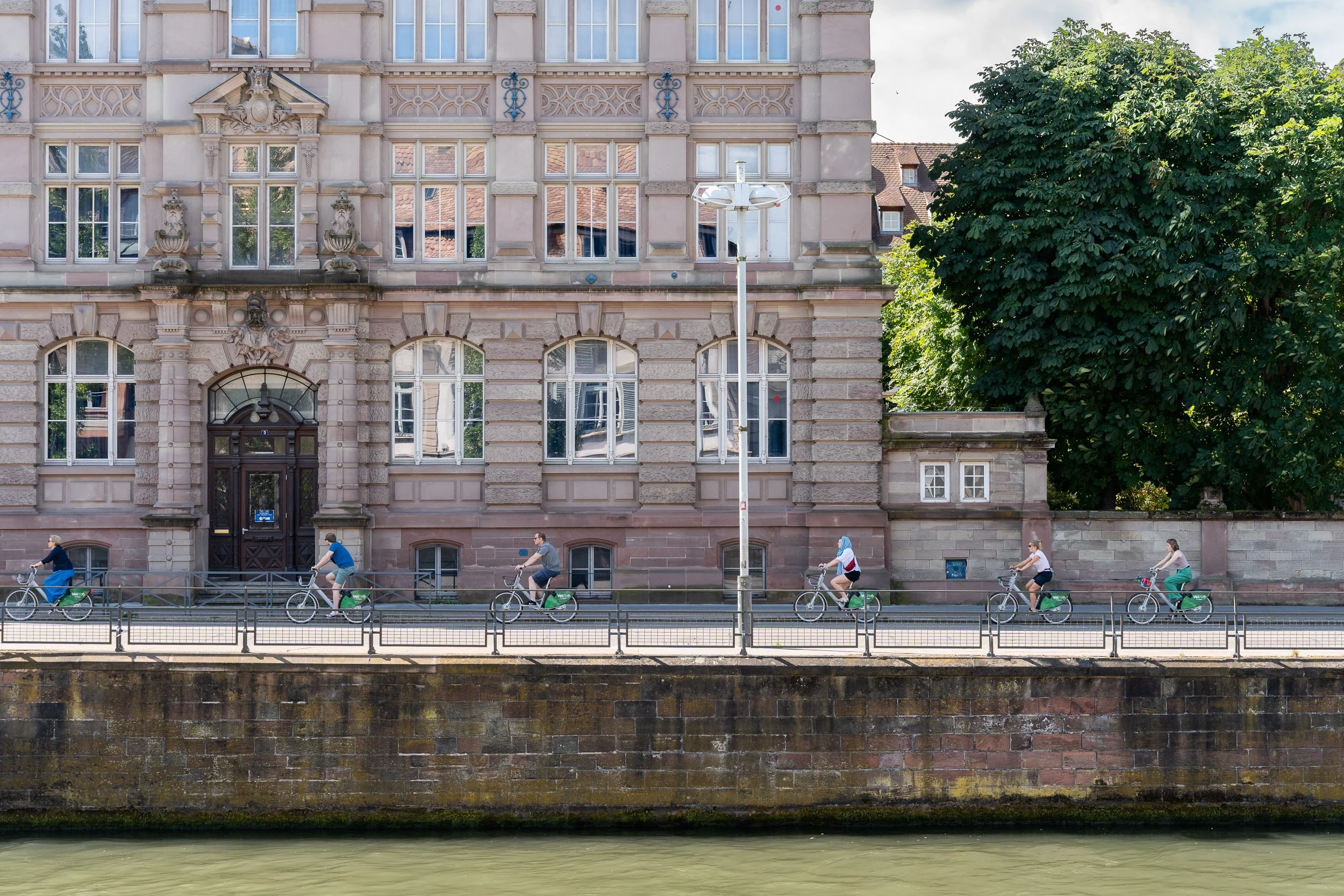 Several cyclists riding in a row along a riverside street in Strasbourg.