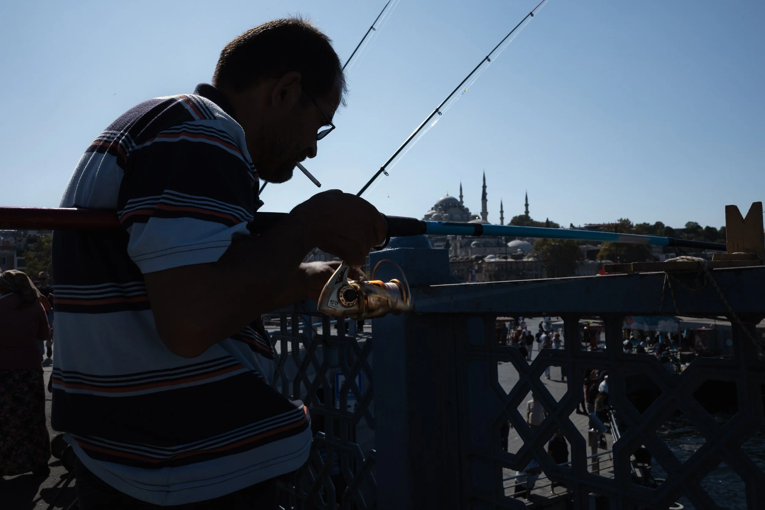 Silhouetted fisherman on a bridge with an Istanbul mosque and minarets in the distance.