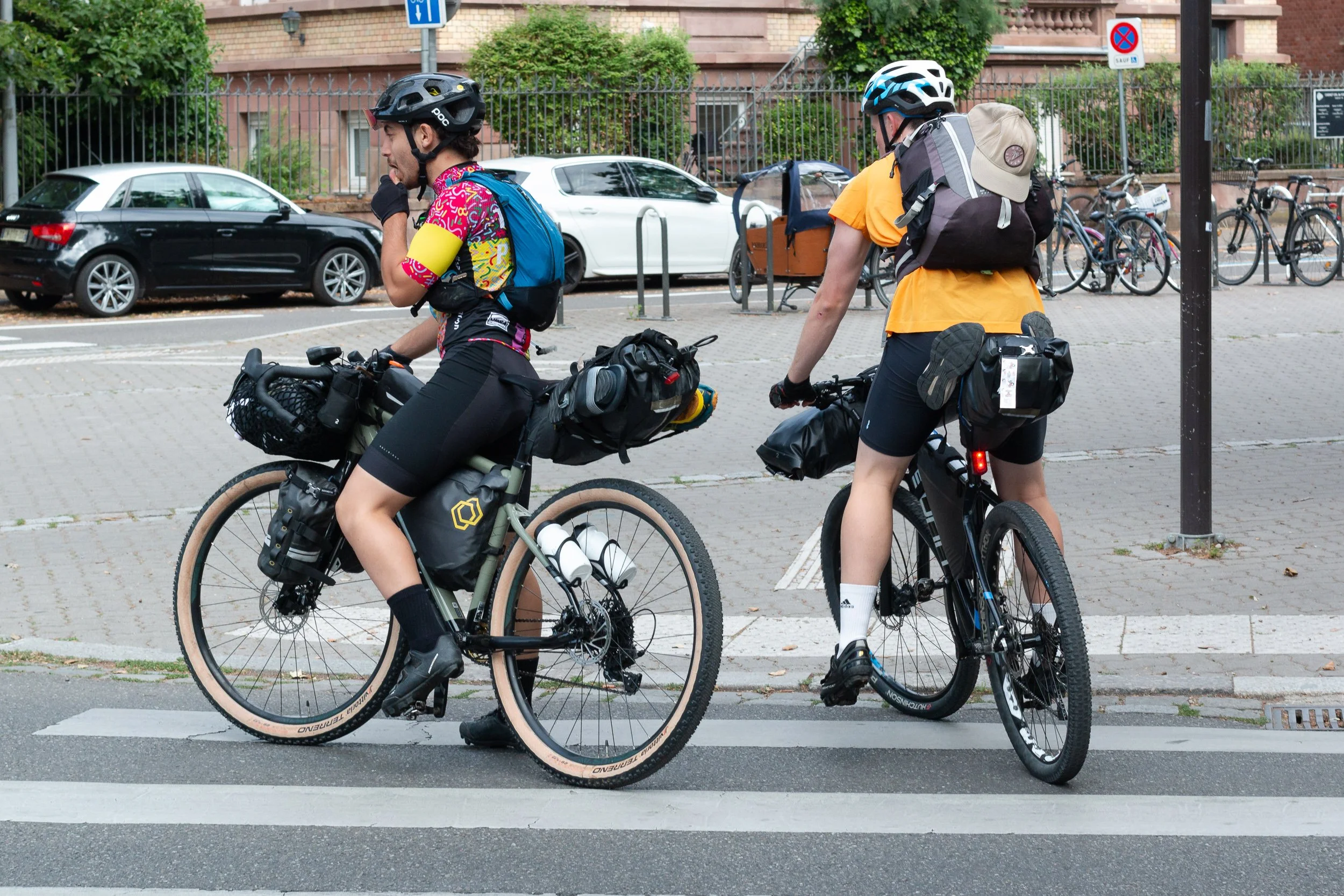 Two touring cyclists with heavily loaded bicycles waiting at a crossing.