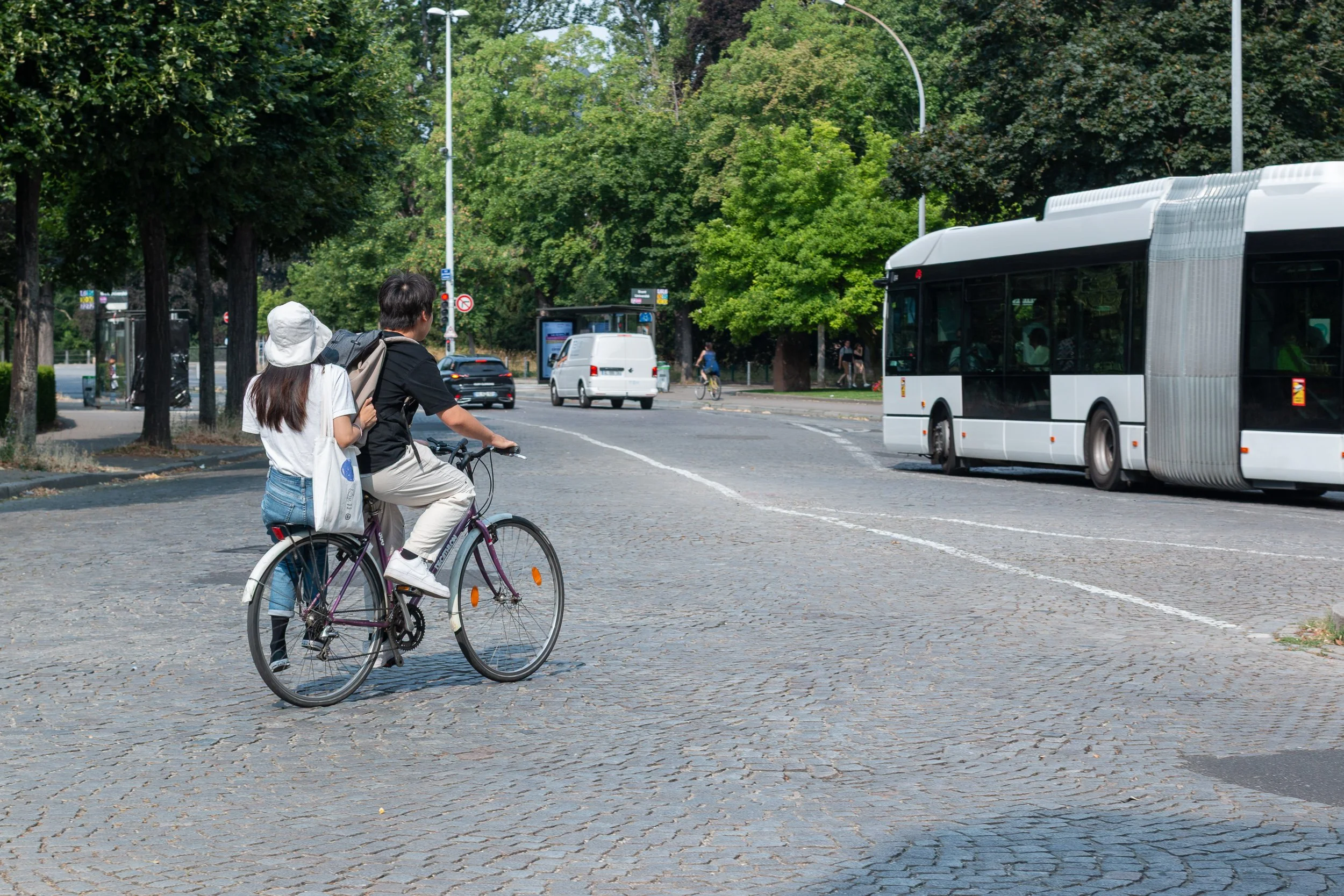 Two people riding together on a bicycle beside a city bus in Strasbourg.