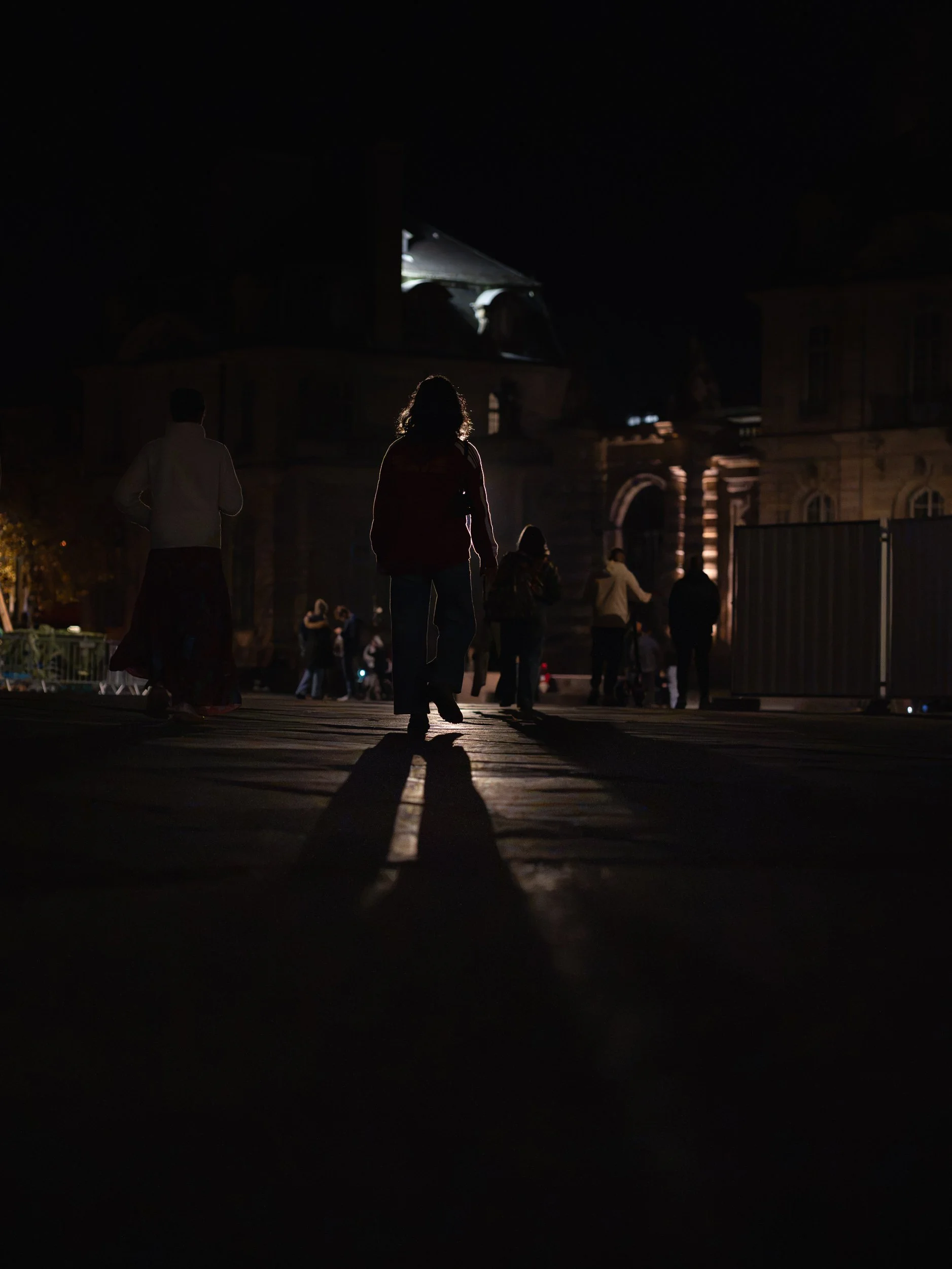 Night pedestrians casting long shadows across a Strasbourg square.