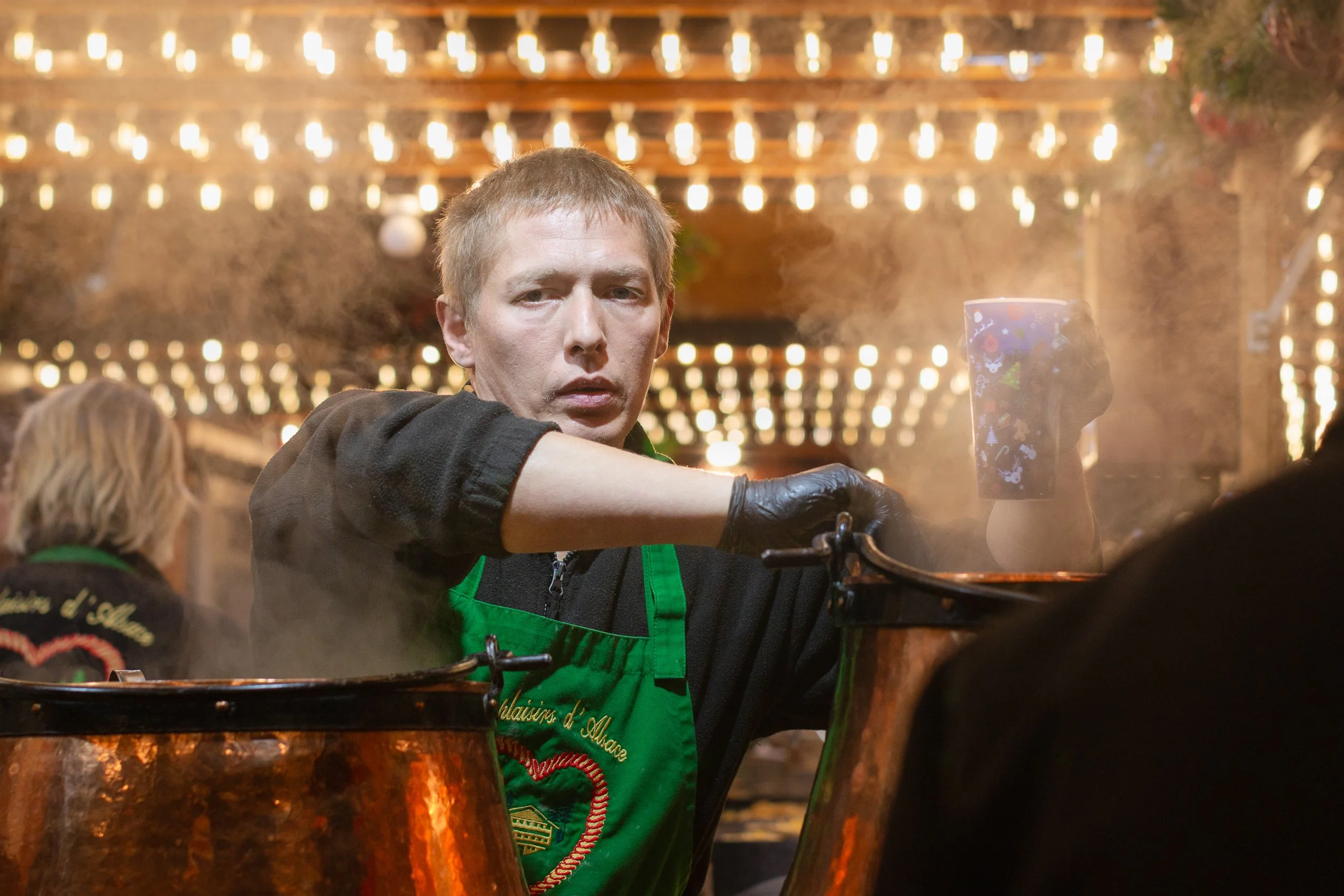 Market vendor stirring a steaming copper pot at a Strasbourg Christmas market.