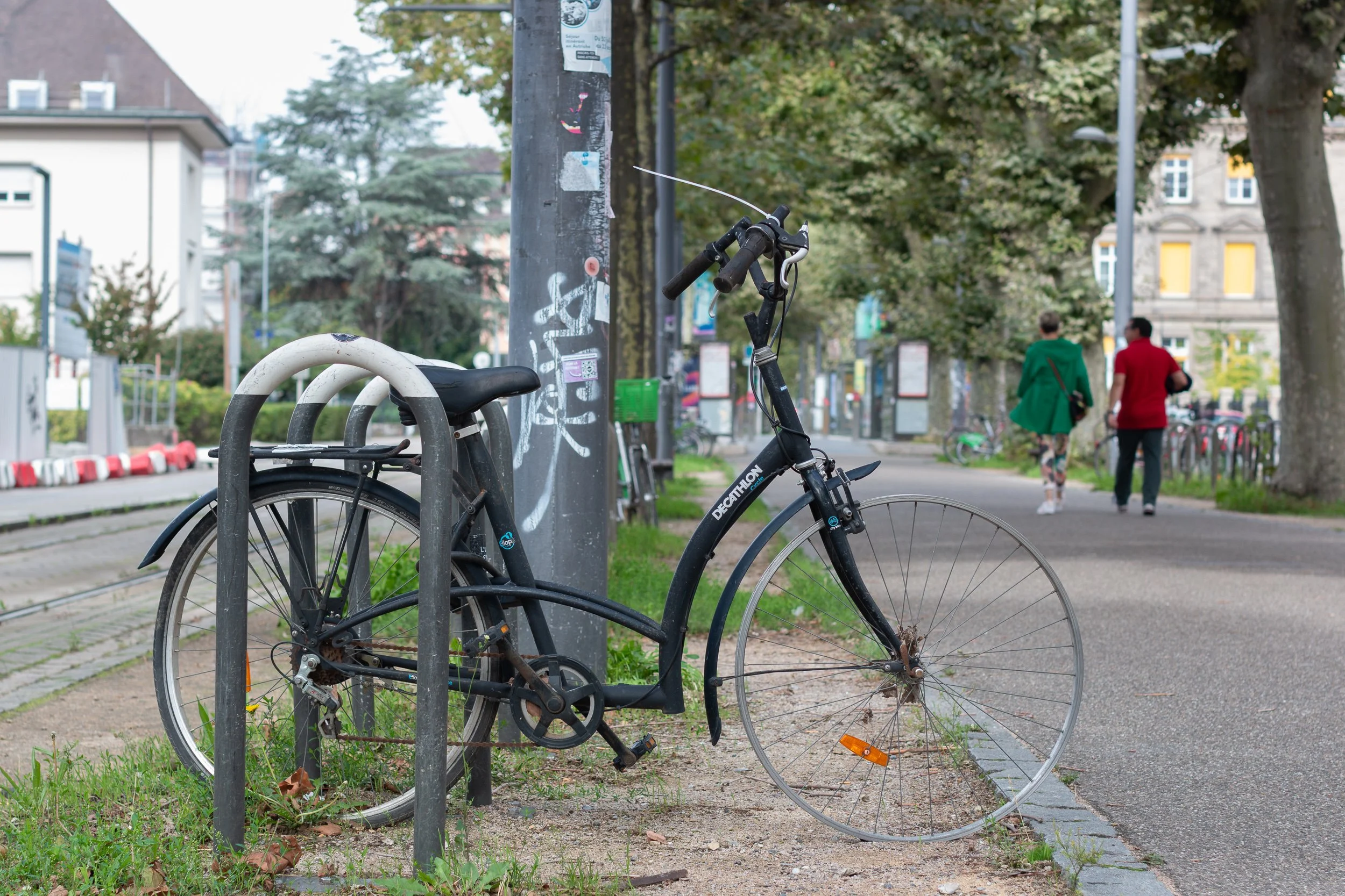 Damaged bicycle locked to a street rack along a Strasbourg cycle path.