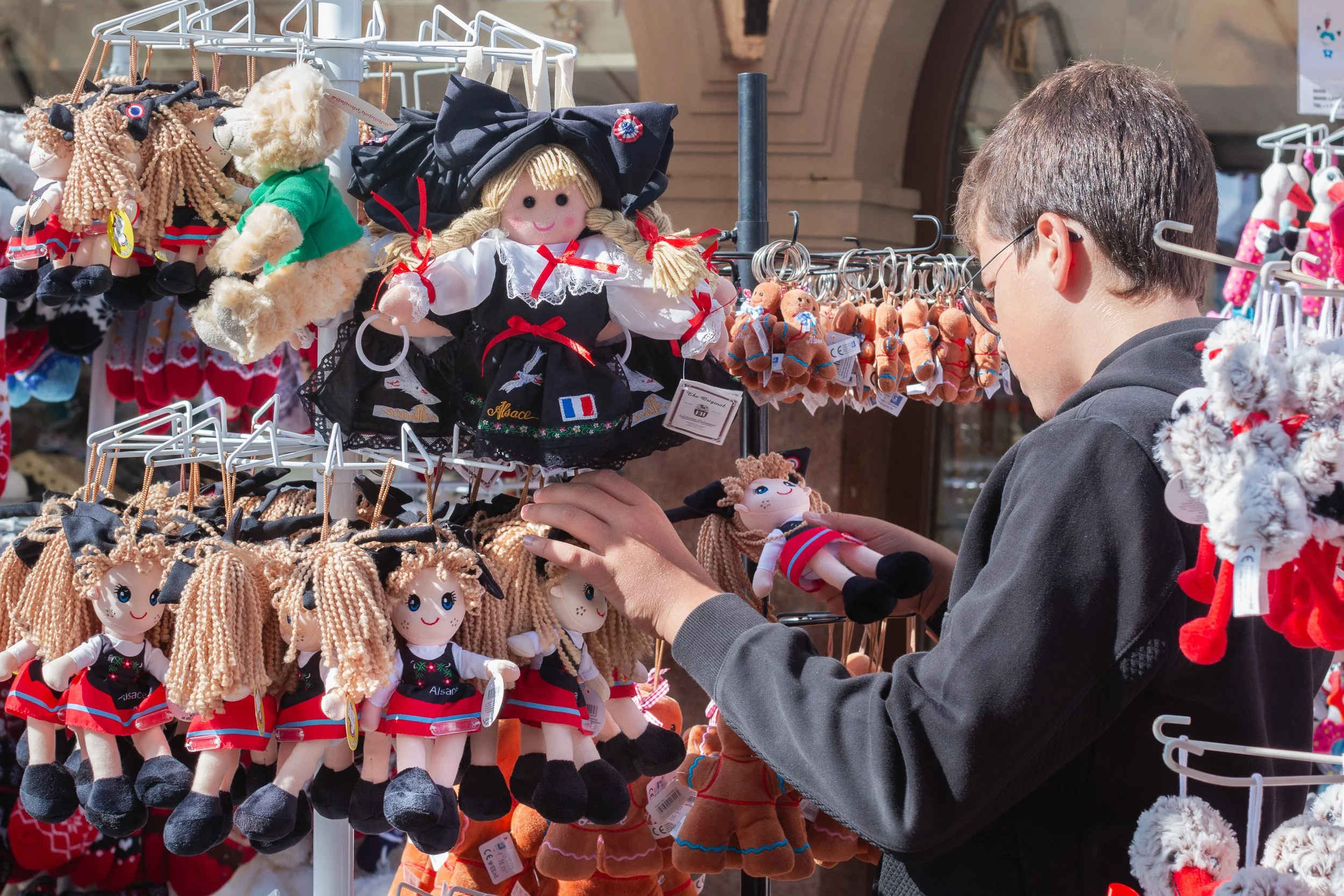 Young visitor choosing traditional Alsatian dolls at a souvenir stand.