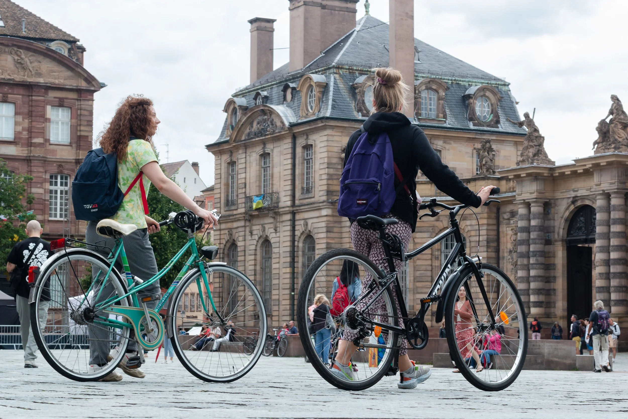 Two women walking their bicycles through a busy square in central Strasbourg.