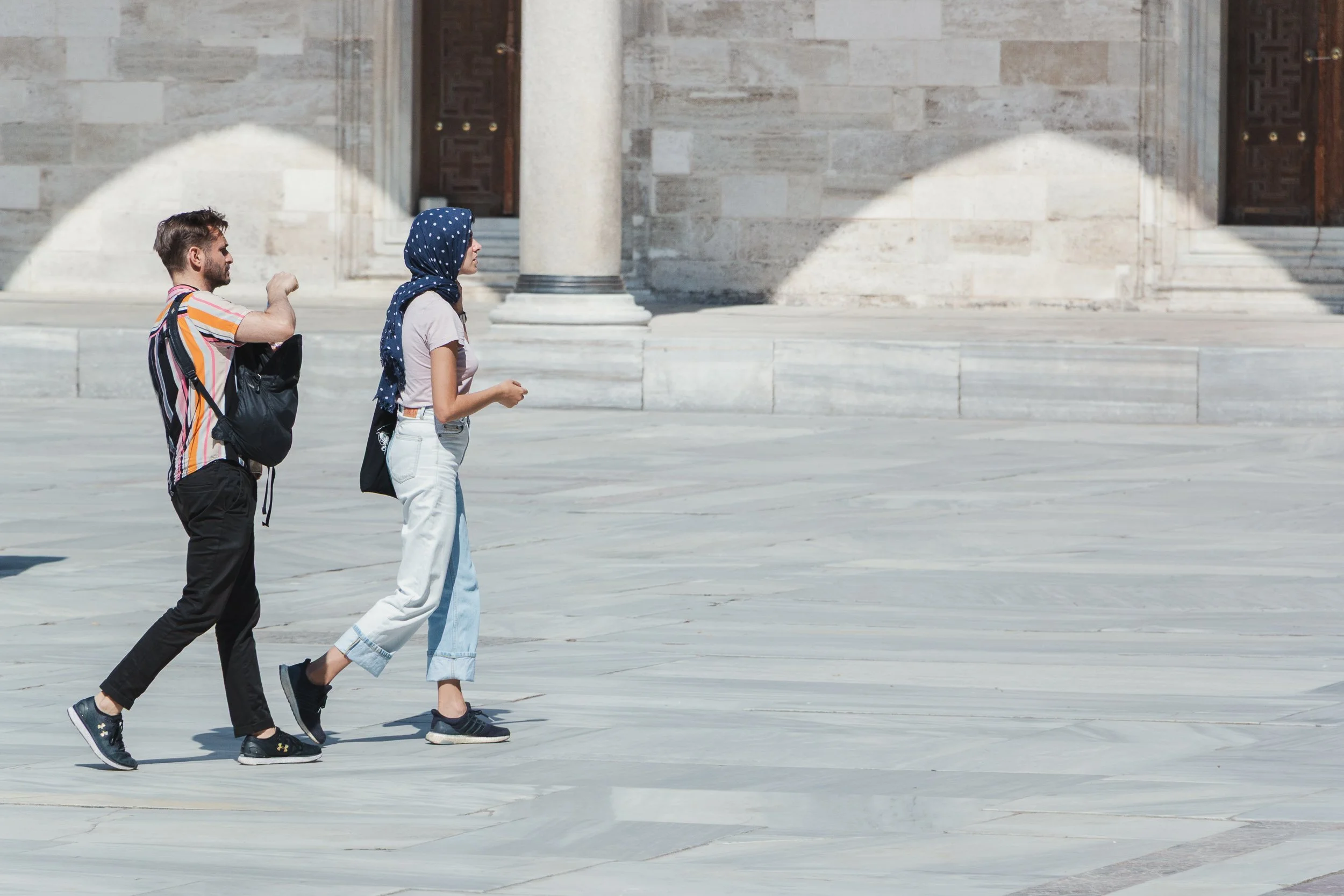 Two pedestrians walking across the sunlit courtyard of a mosque in Istanbul.