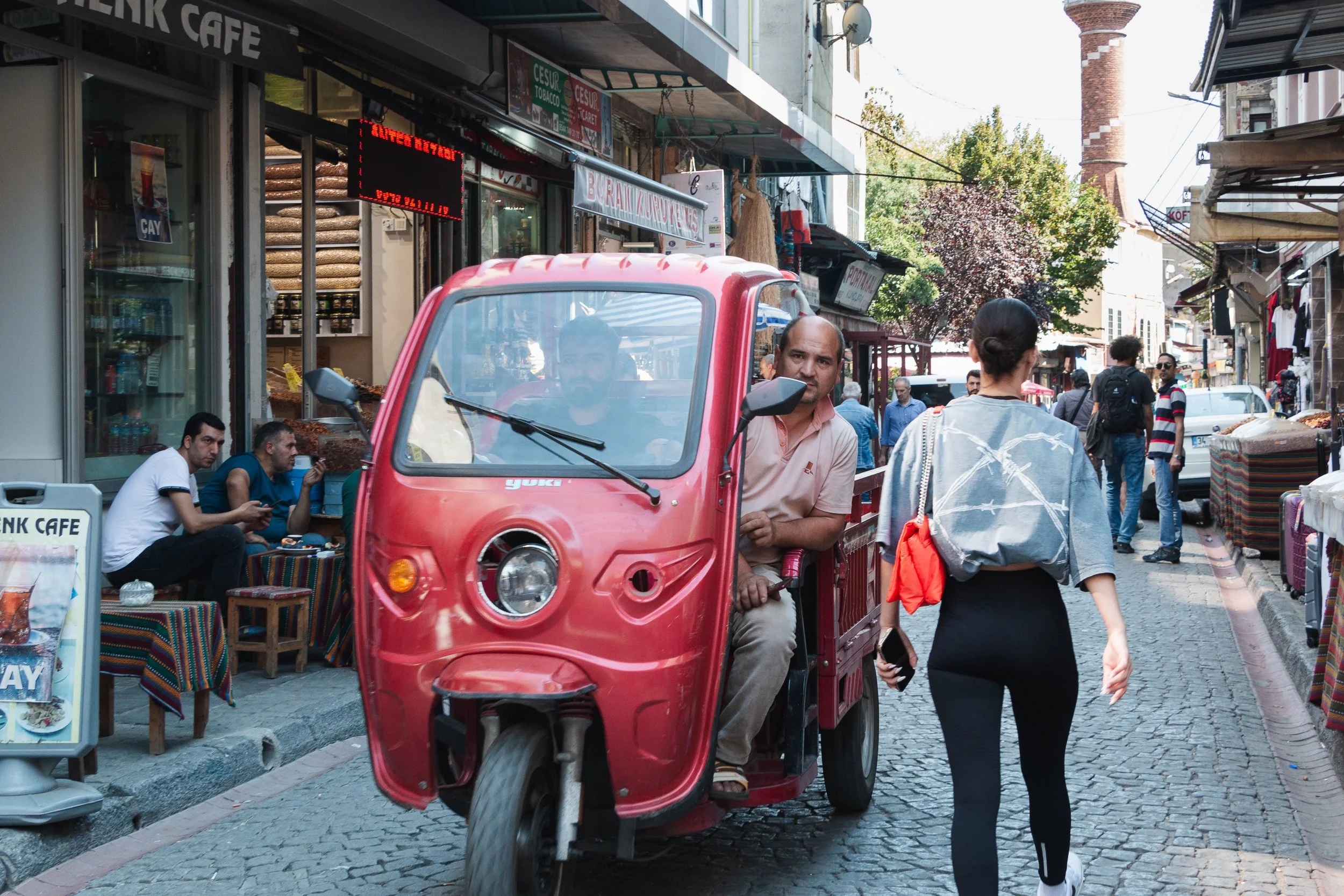 Red three-wheeled vehicle passing a pedestrian on a narrow, busy street in Istanbul.