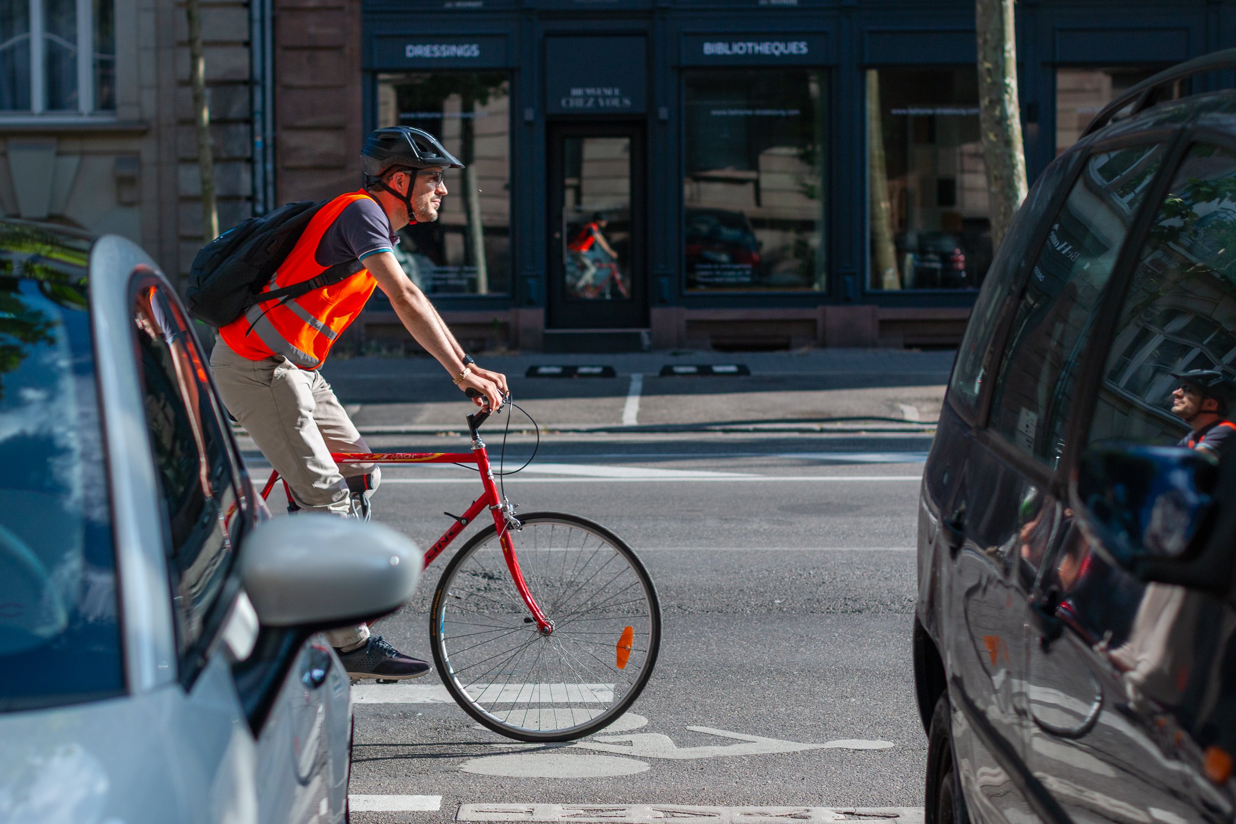Cyclist riding between parked cars on a marked bicycle lane in Strasbourg.