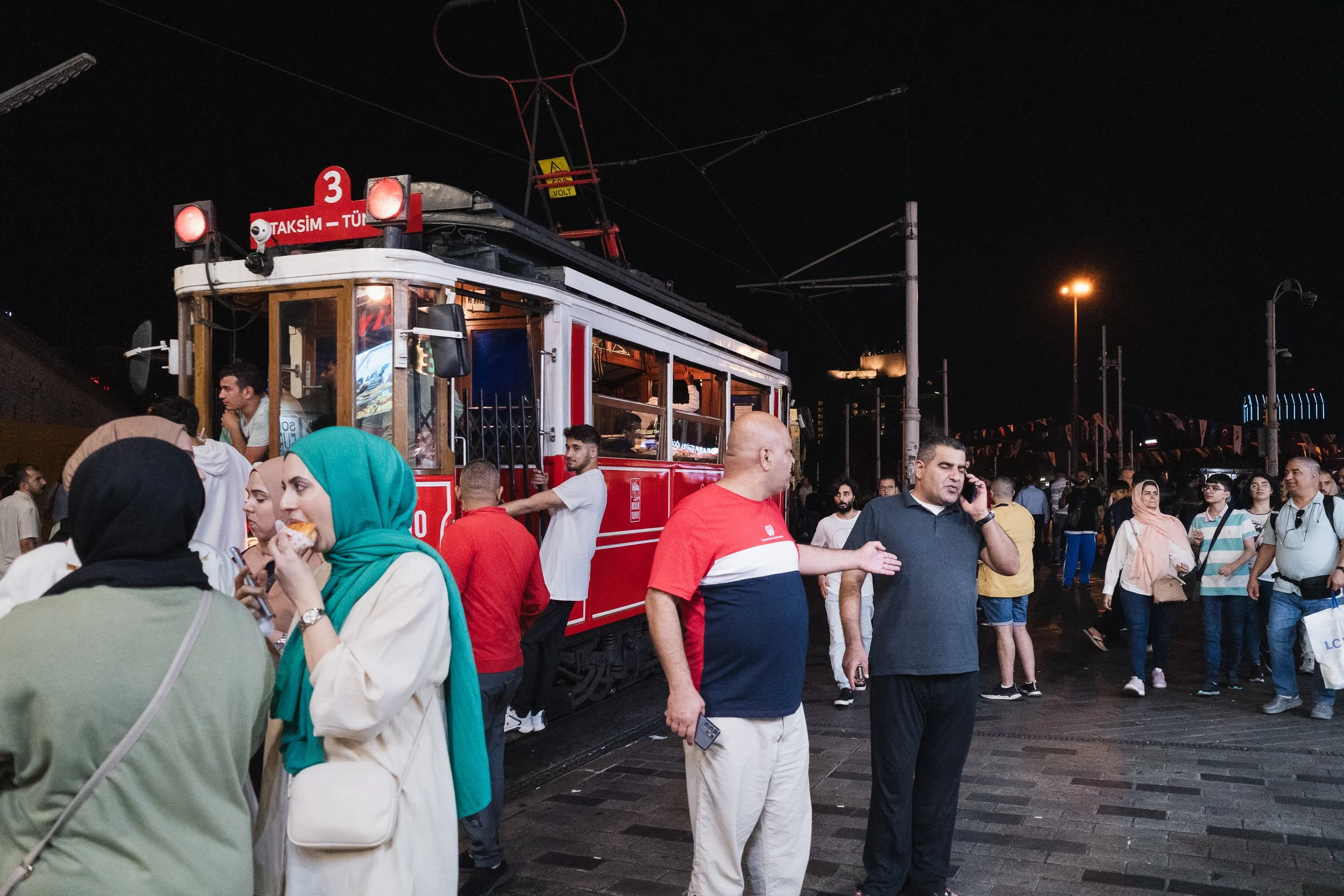 Crowds gathered around the historic red tram in Istanbul at night.