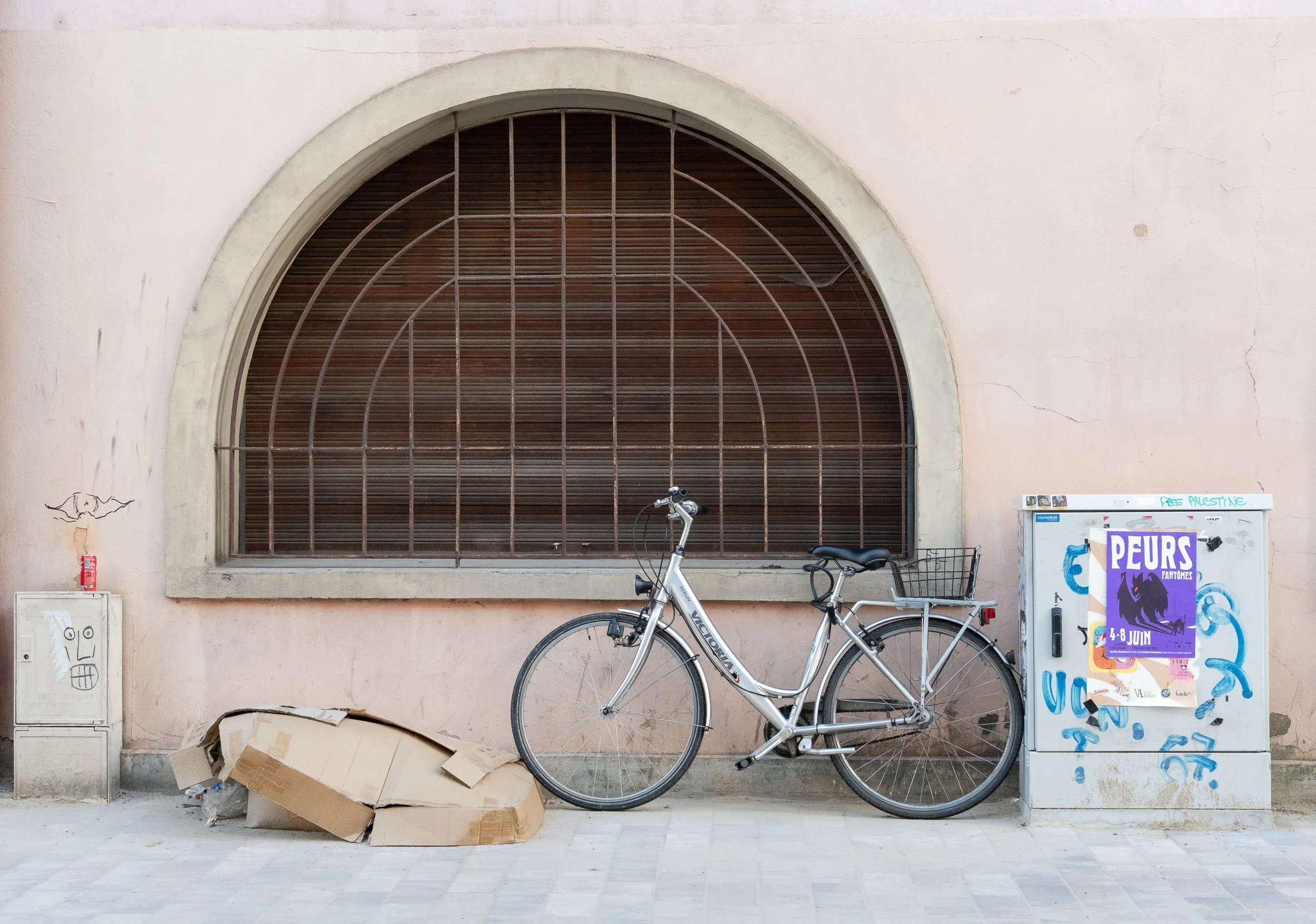 Bicycle parked against a wall beside cardboard and a graffiti-covered utility box.