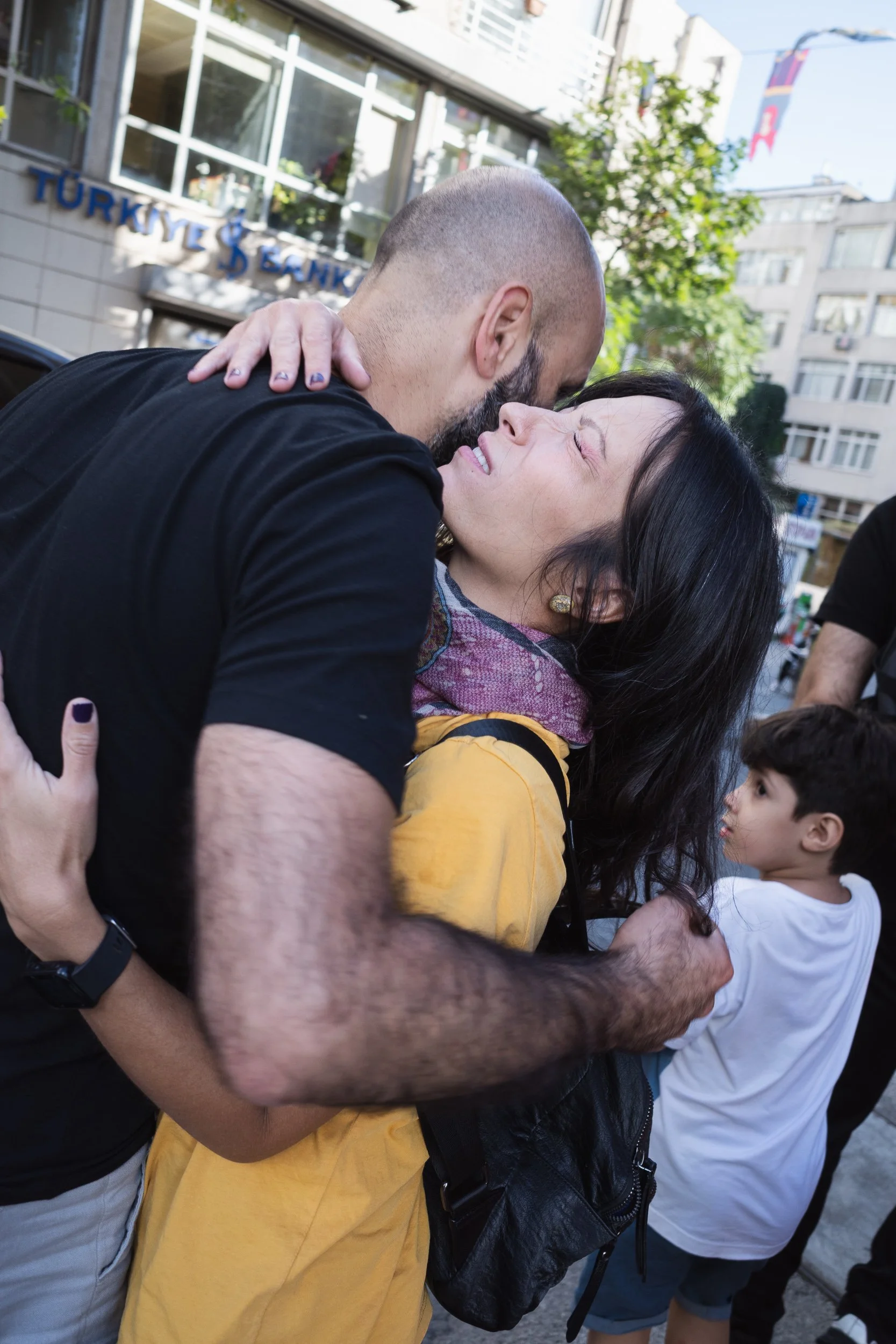 Man and woman embracing in a crowded Istanbul street while a child looks on.