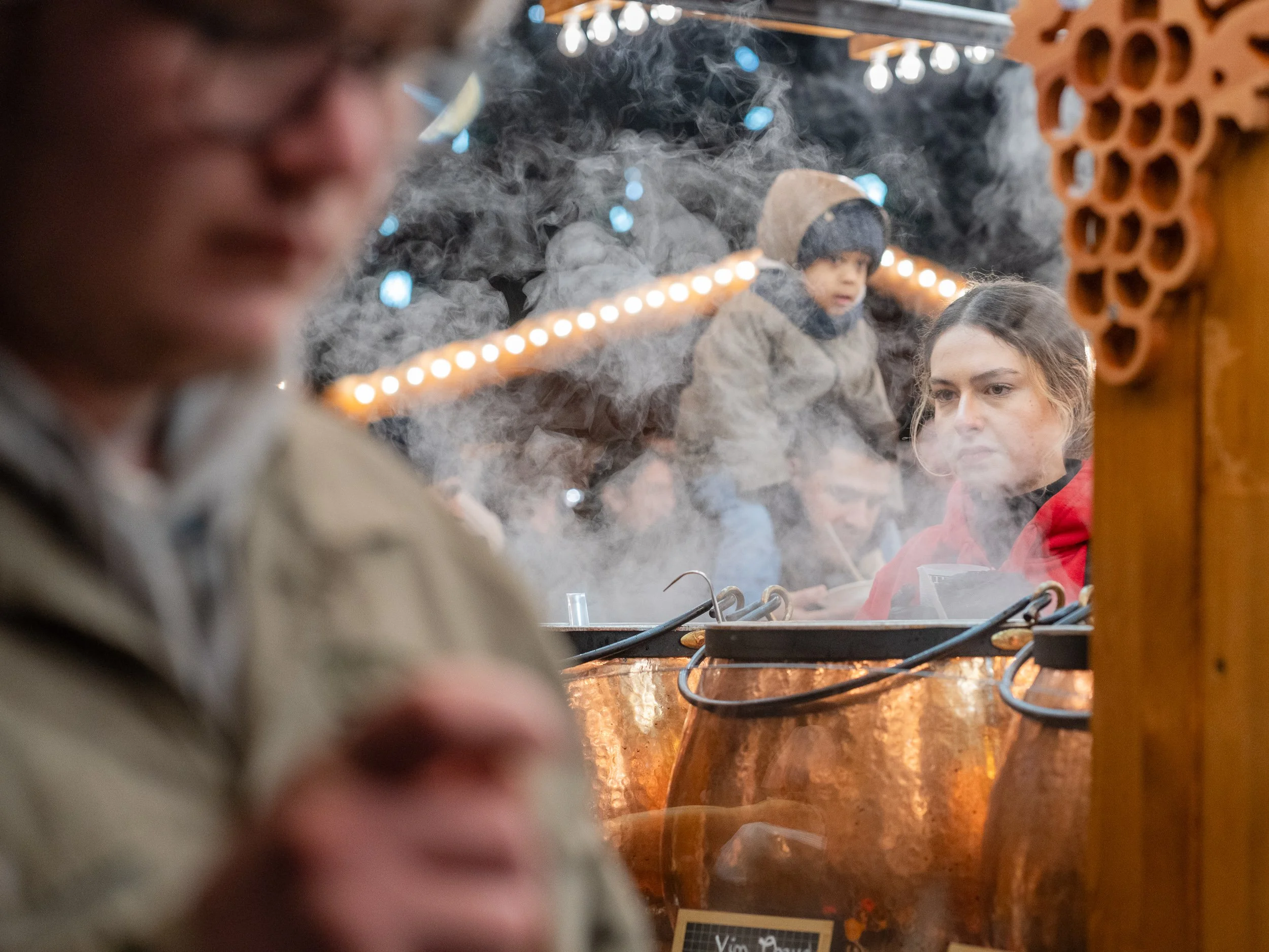 Woman in a red coat seen through steam at a Strasbourg market stall.
