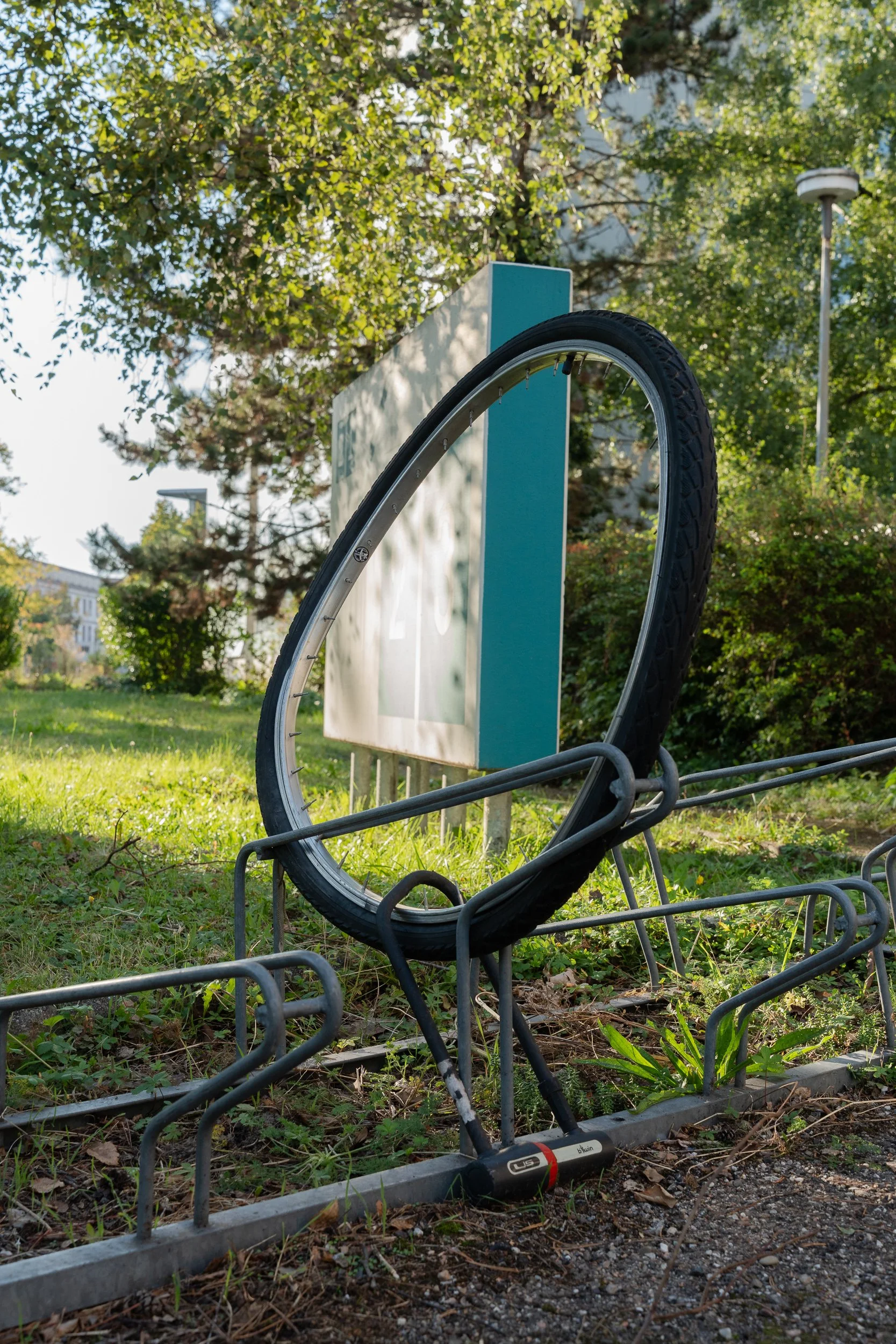 Single bicycle wheel and tyre locked to an empty bike rack.