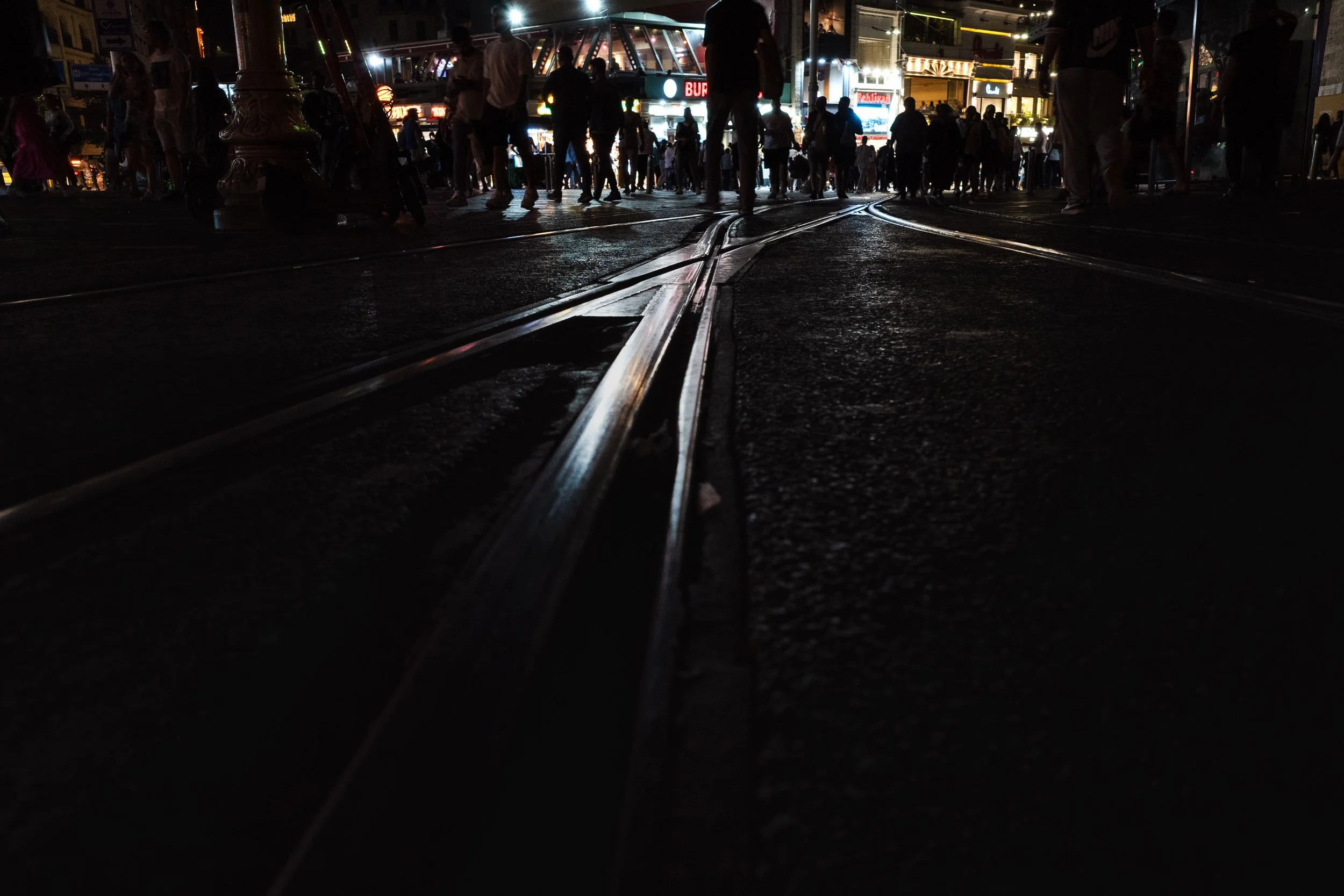 Tram tracks leading toward a crowd and city lights on a busy Istanbul street at night.