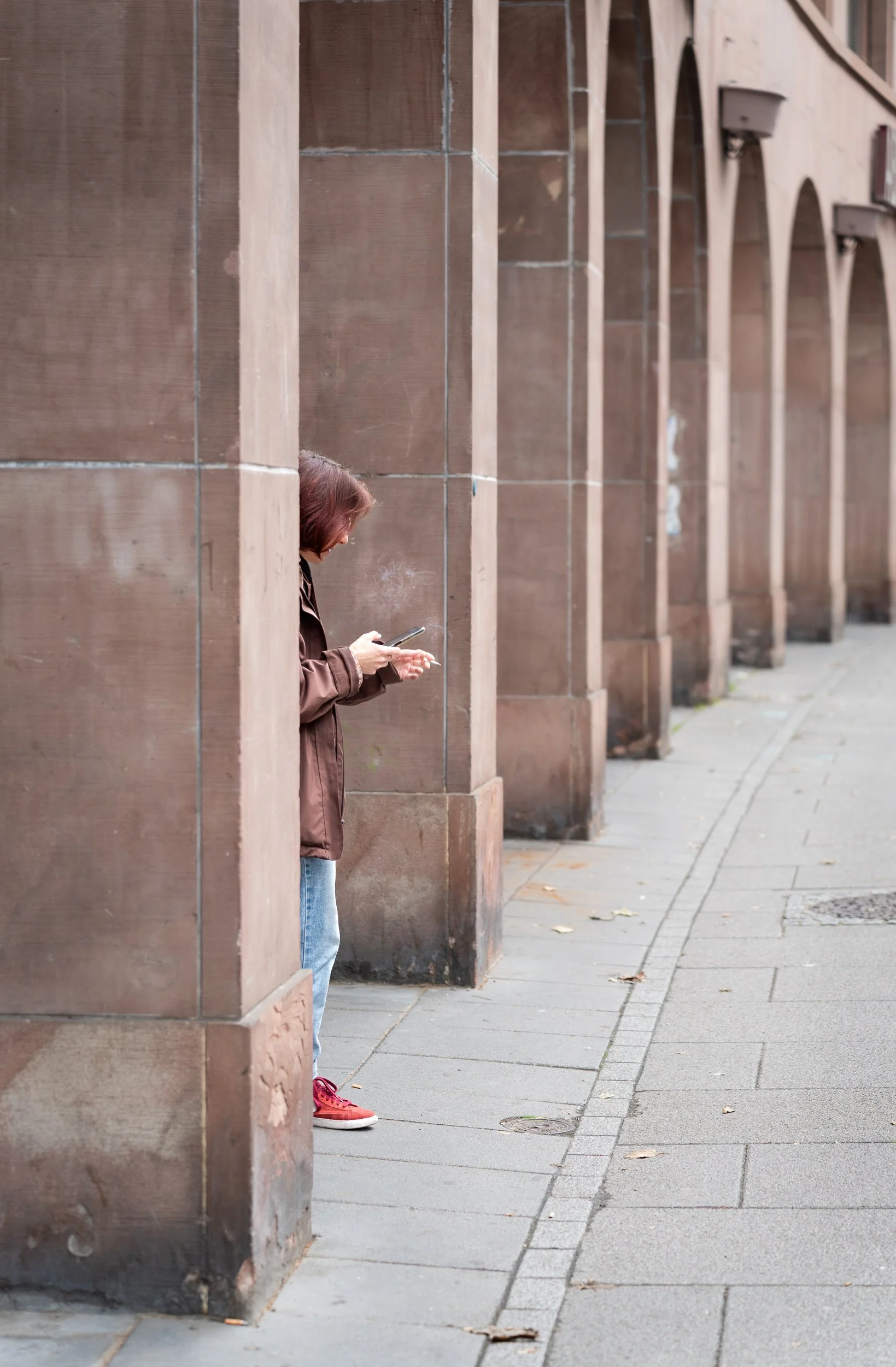 Woman smoking and checking her phone between stone columns in Strasbourg.