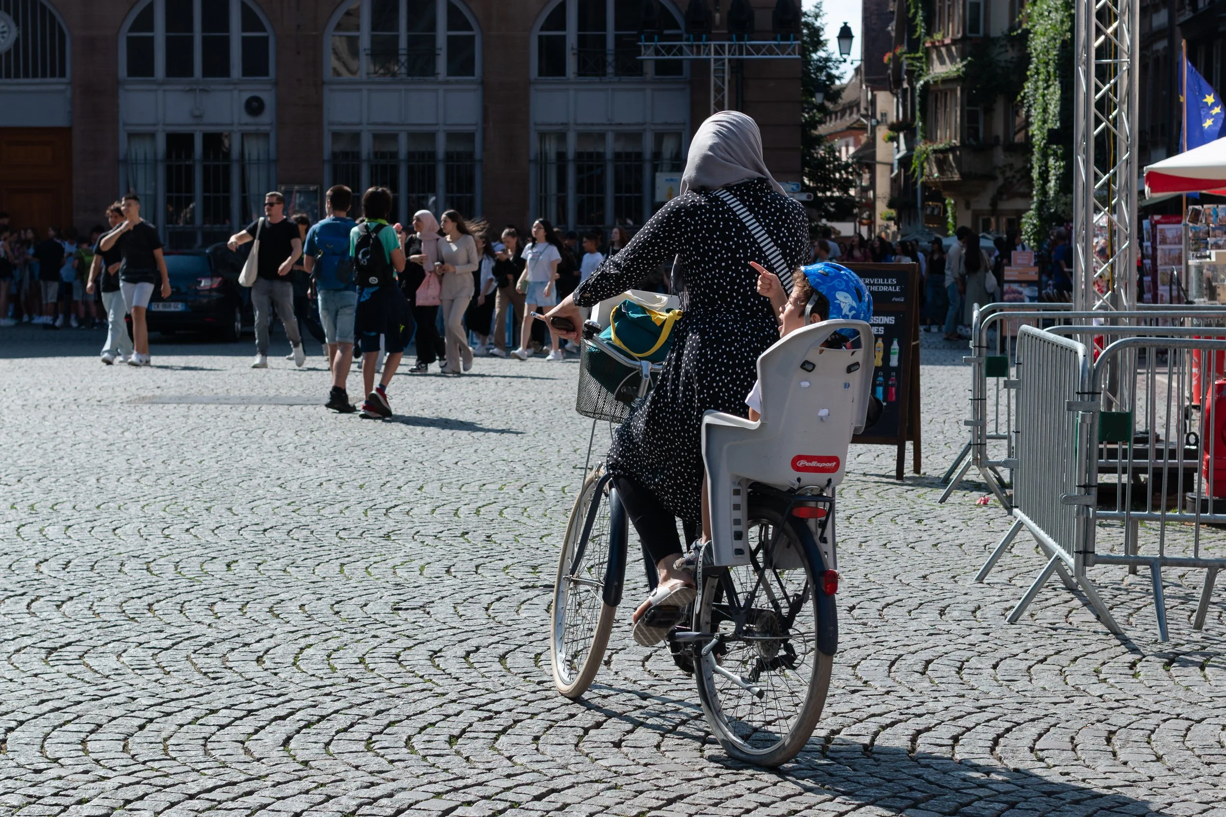 Woman cycling through a busy square with a child seat mounted on the bicycle.