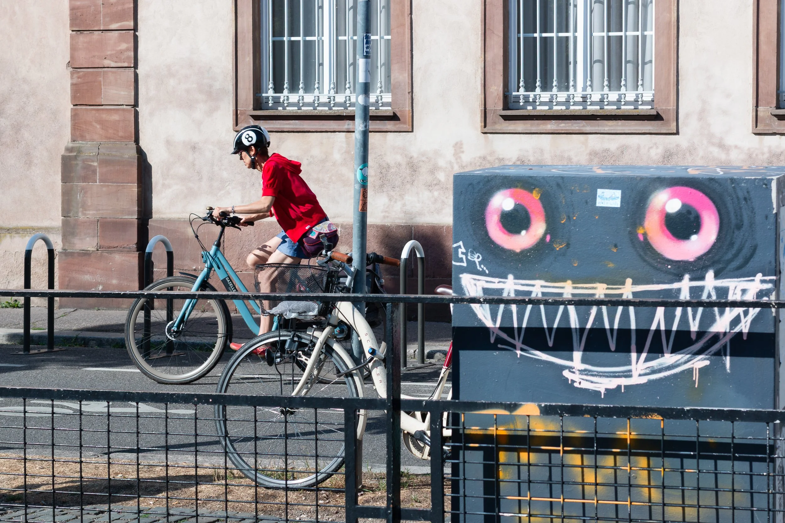Cyclist passing a utility box painted with a large smiling face in Strasbourg.