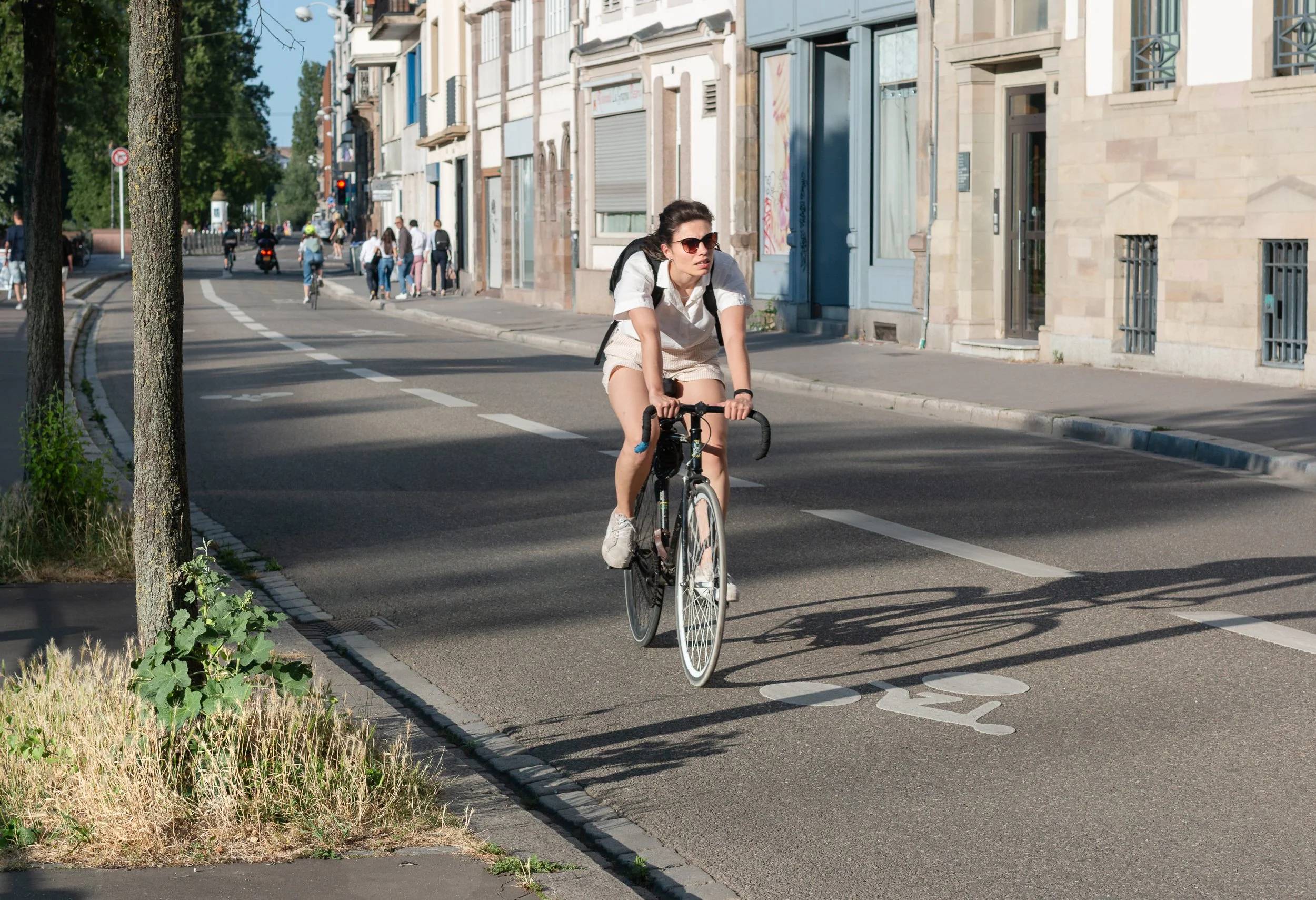 Woman cycling along a marked bike lane on a sunny street in Strasbourg.
