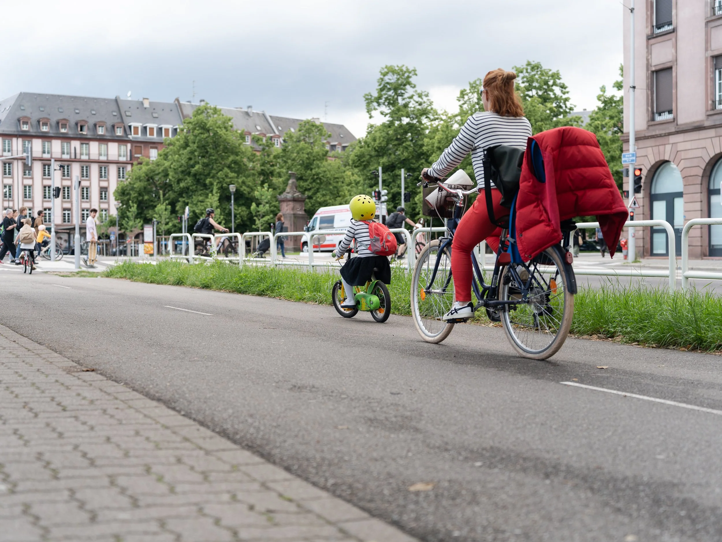 Adult cyclist following a small child riding along a Strasbourg cycle path.