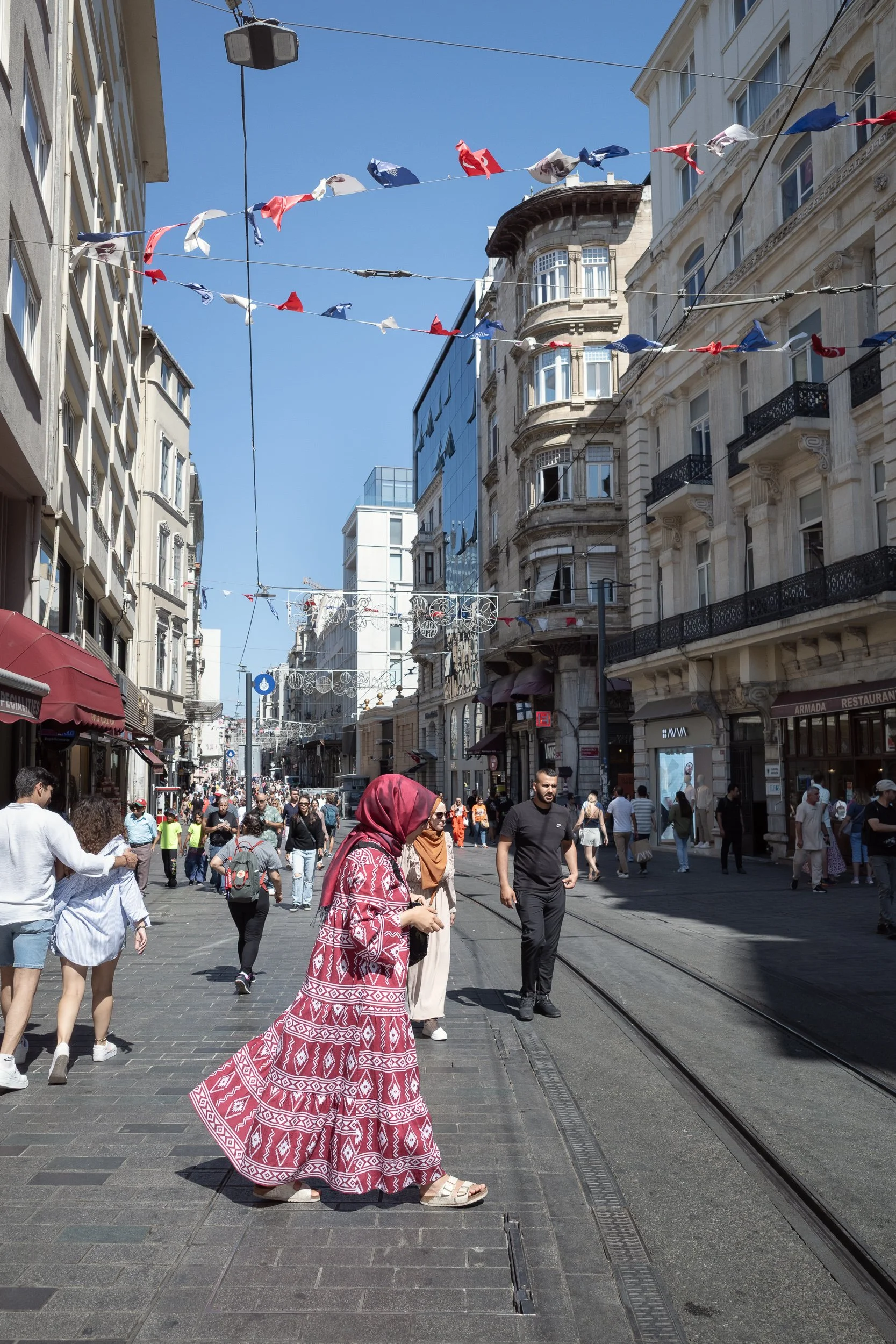 Woman in a red patterned dress crossing a busy pedestrian street beneath hanging flags in Istanbul.