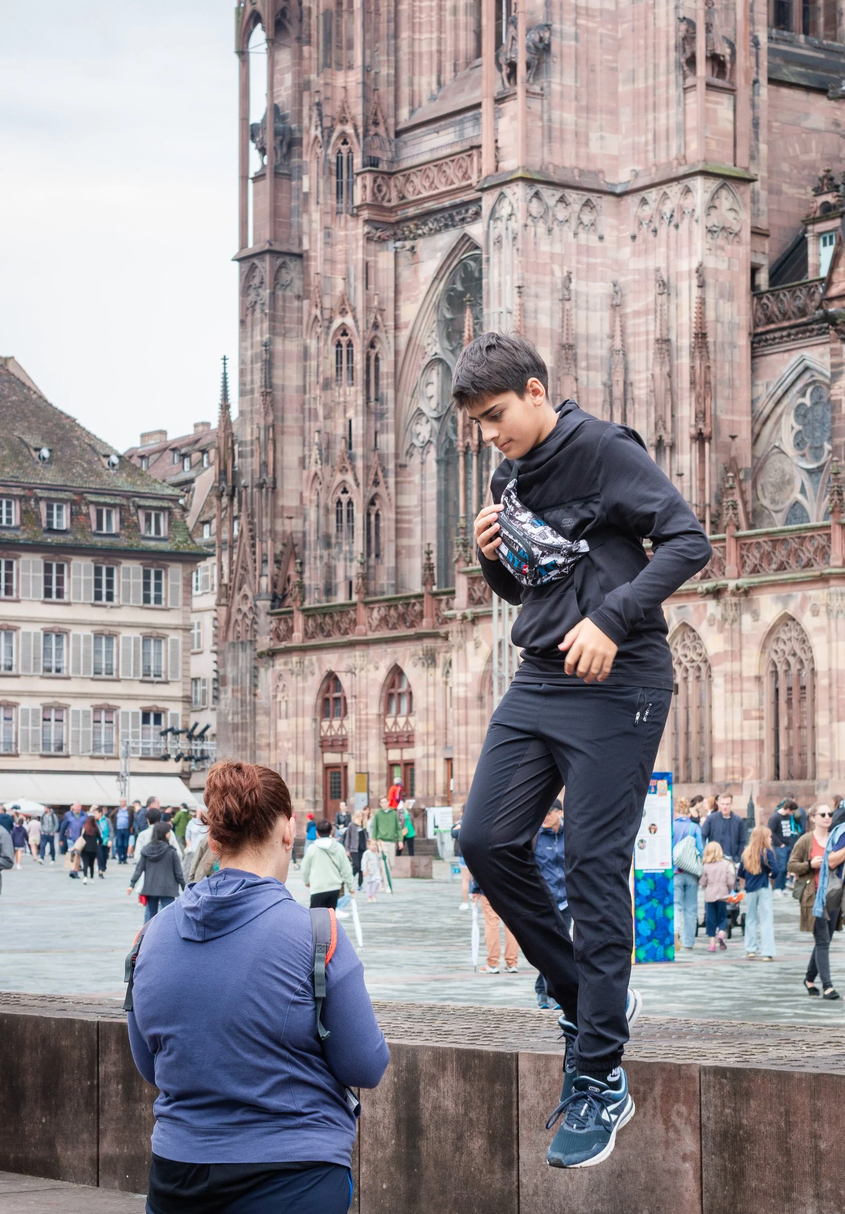 Boy stepping across a low wall in front of Strasbourg Cathedral.