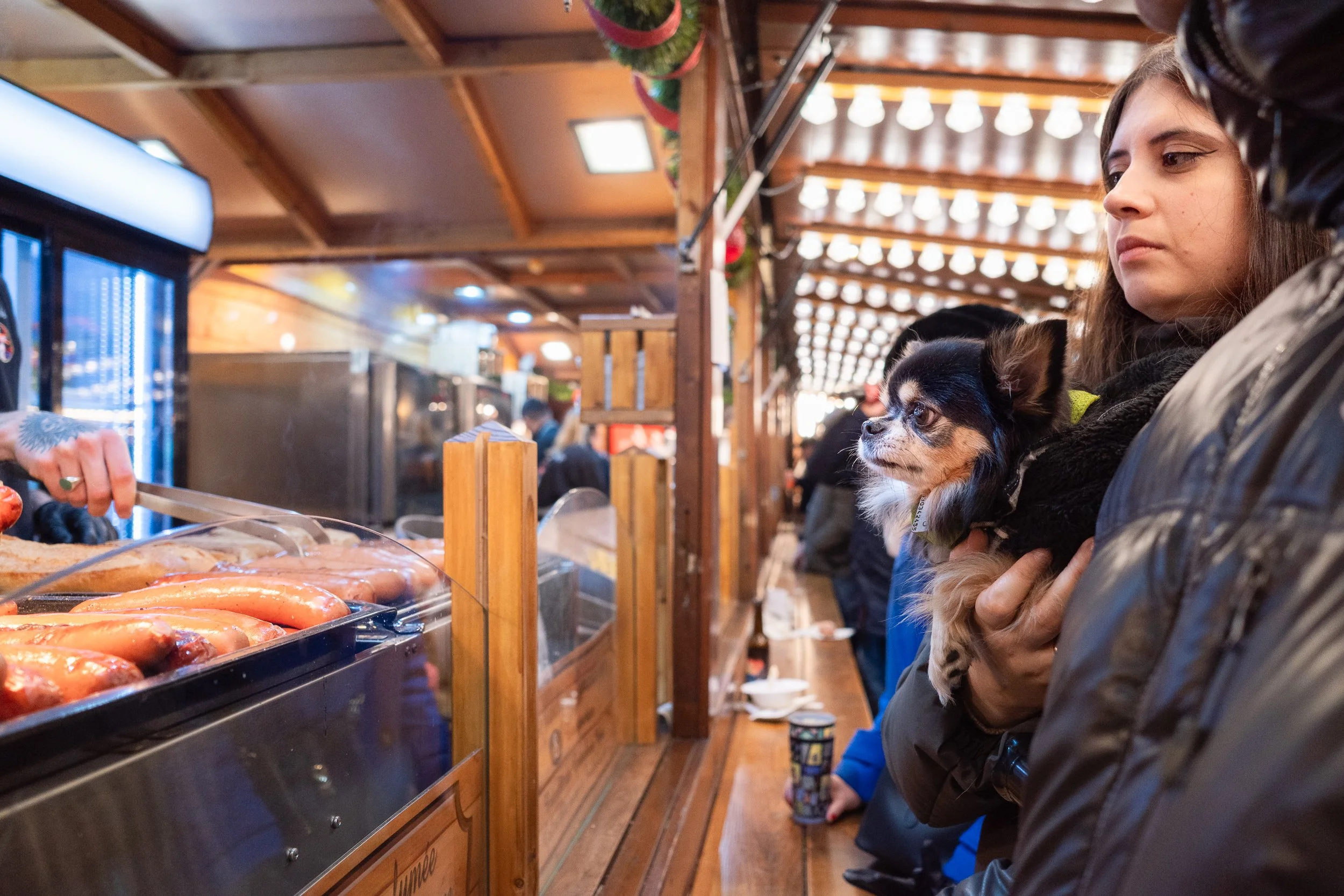 Woman holding a small dog while waiting at a Strasbourg market stall.