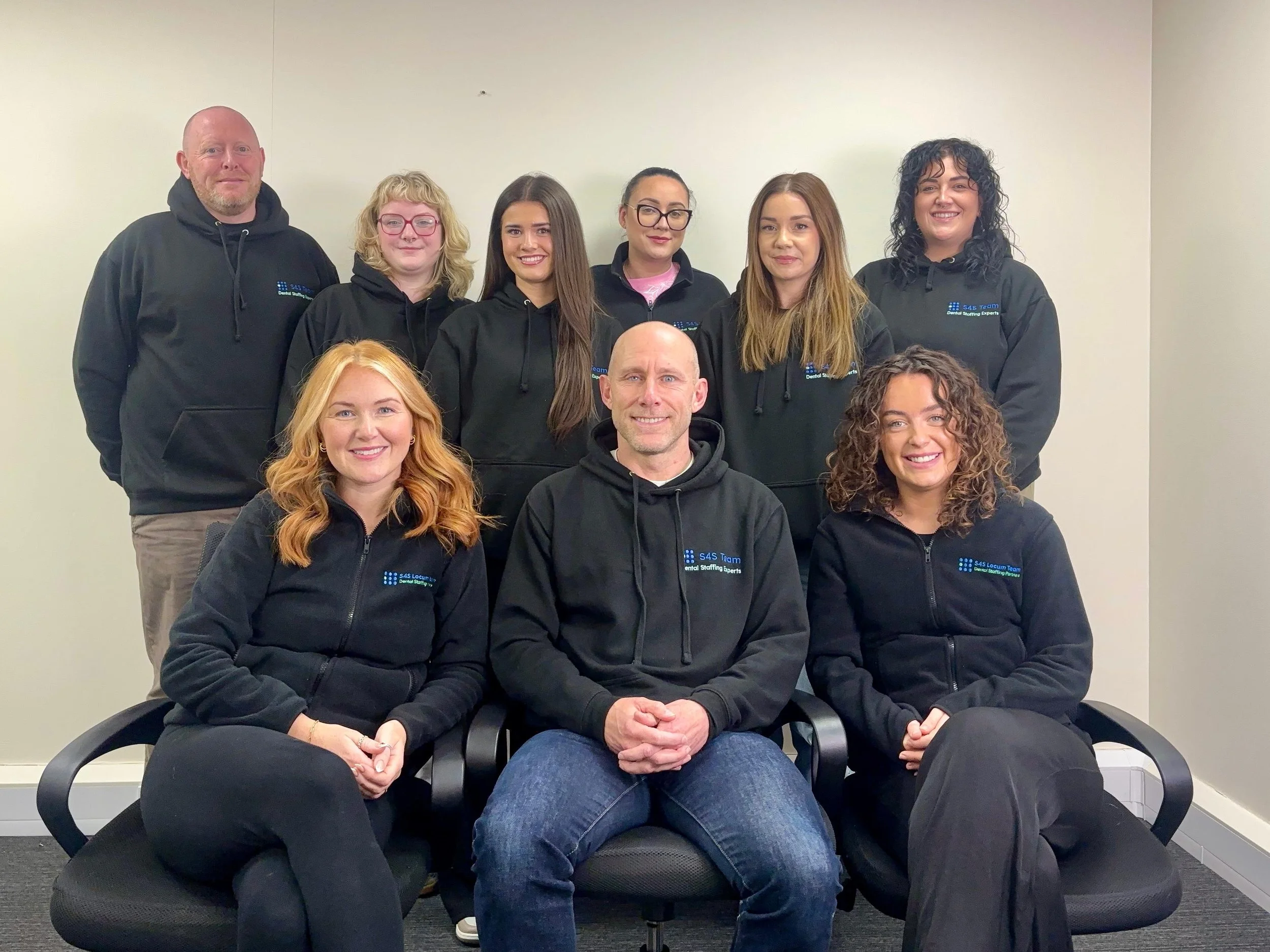 A photo of the whole team together wearing black S4S Locum Team hoodies against a white background