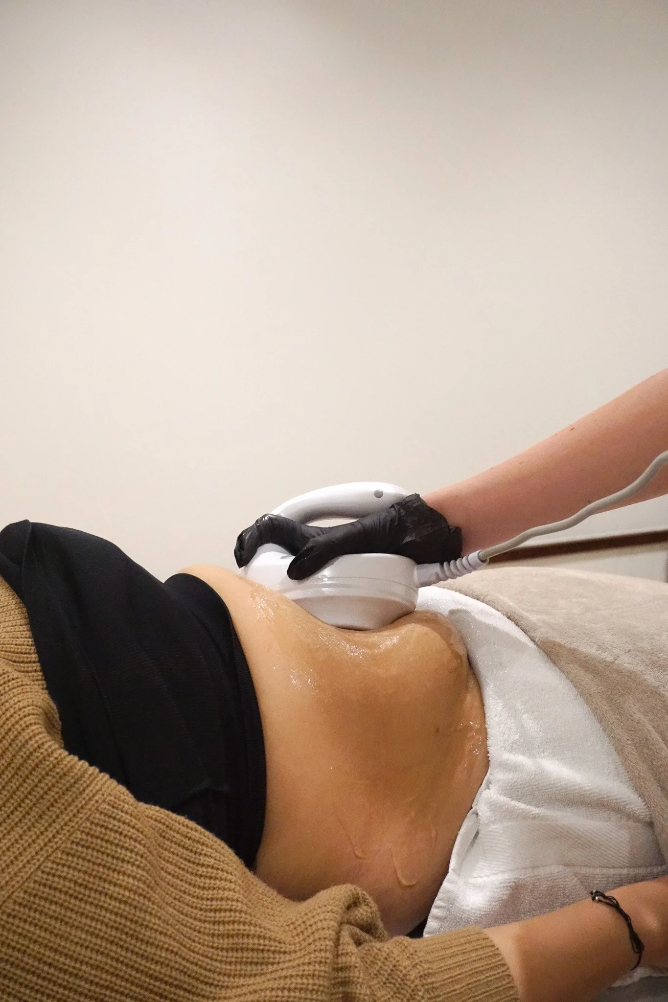 Person receiving a medical ultrasound scan on their abdomen, lying down with an ultrasound probe on their stomach, covered by a white towel.