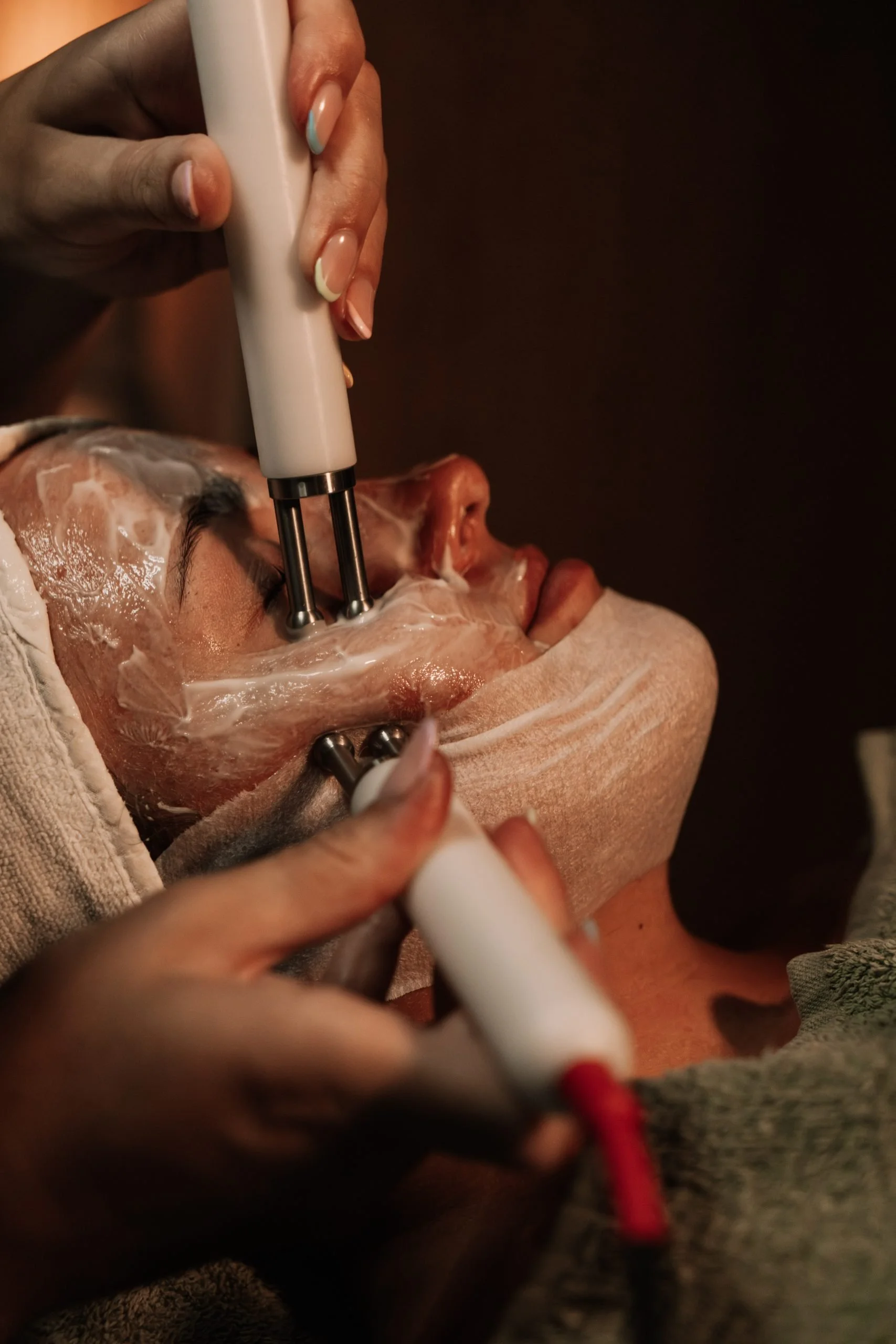 Person receiving a facial treatment with a facial machine and a mask applied to their face.