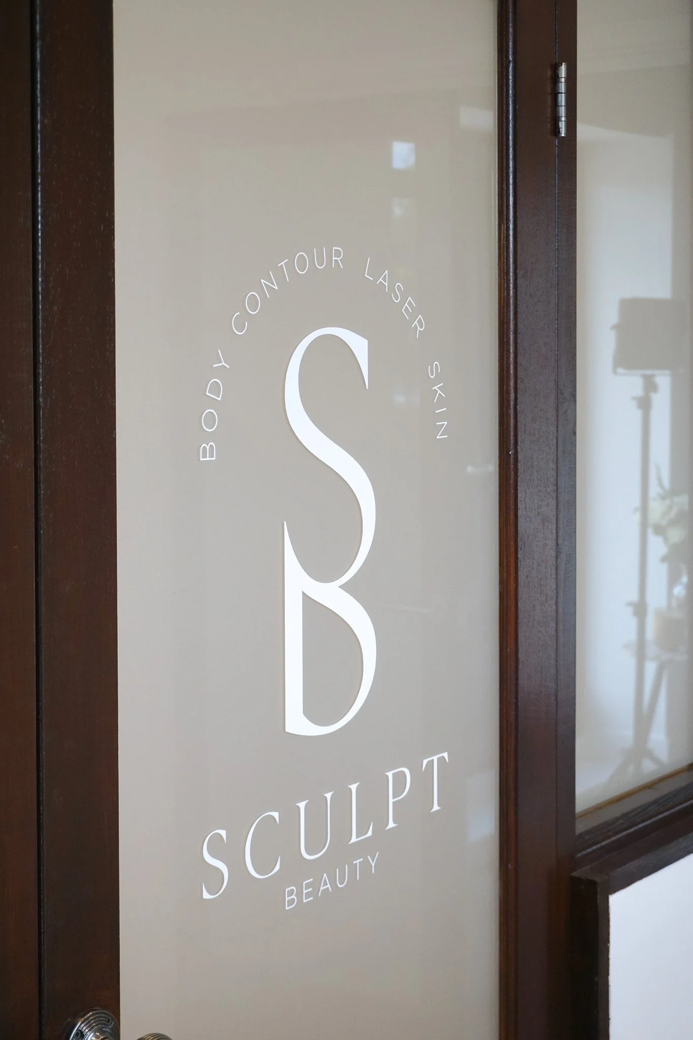 Close-up of a door with the sign reading "Body Contour Laser Skin Sculpt Beauty" in white letters on a beige background with dark wood framing.