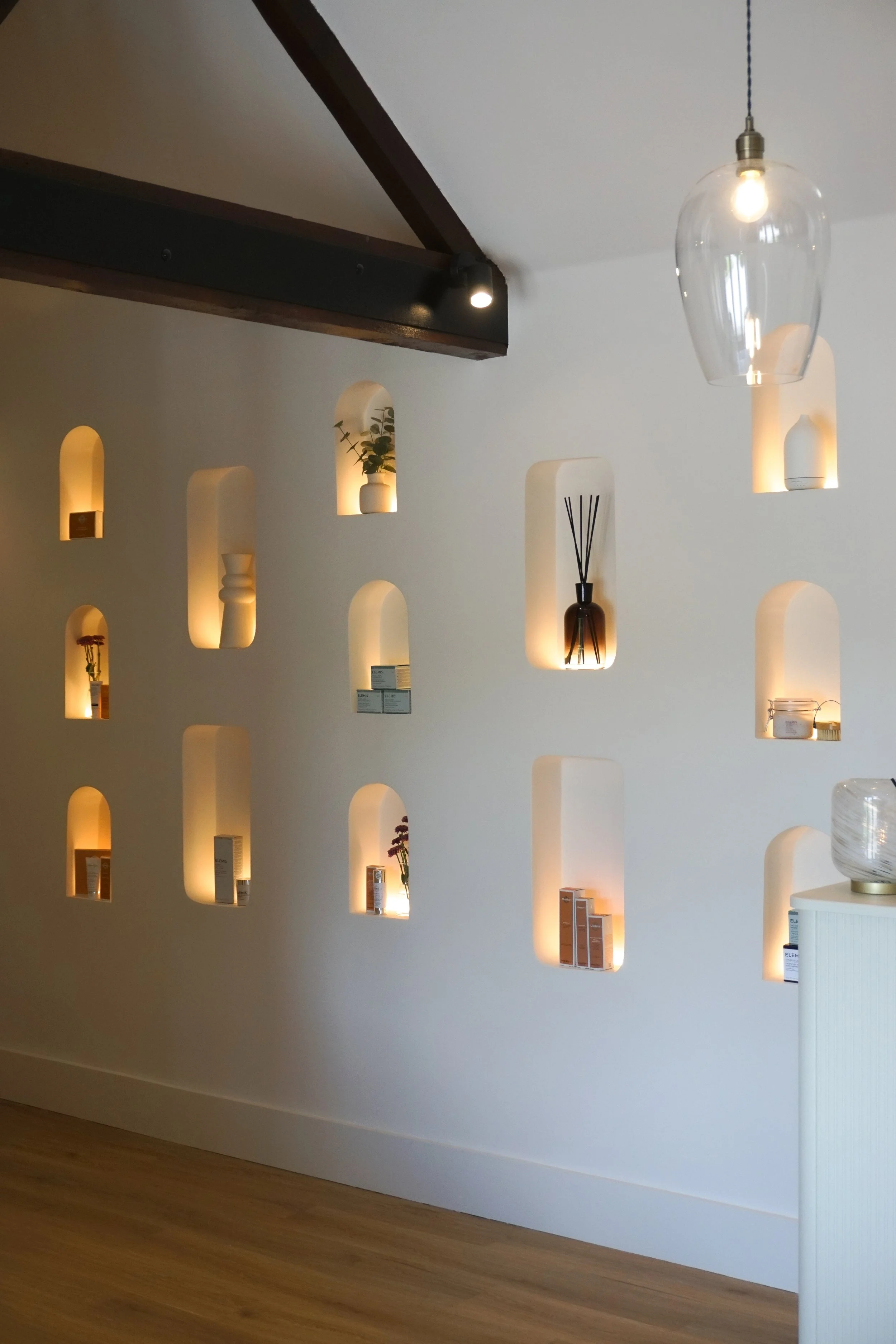 A wall with built-in illuminated niches containing various vases, plants, and decorative items in a modern interior space.